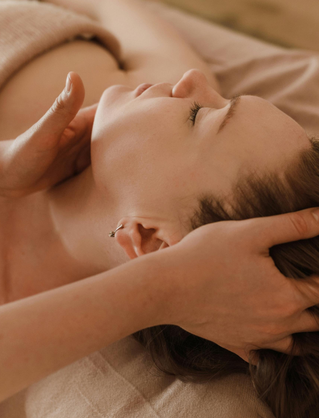 A woman receiving a massage, lying on her back with her eyes closed, on a massage table.