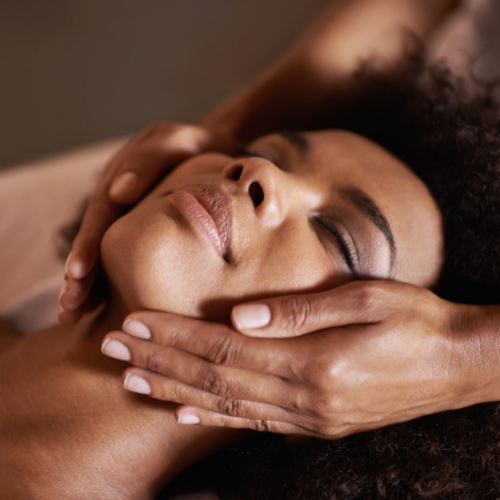 Close-up of a woman receiving a relaxing massage with hands gently cradling her face and neck.