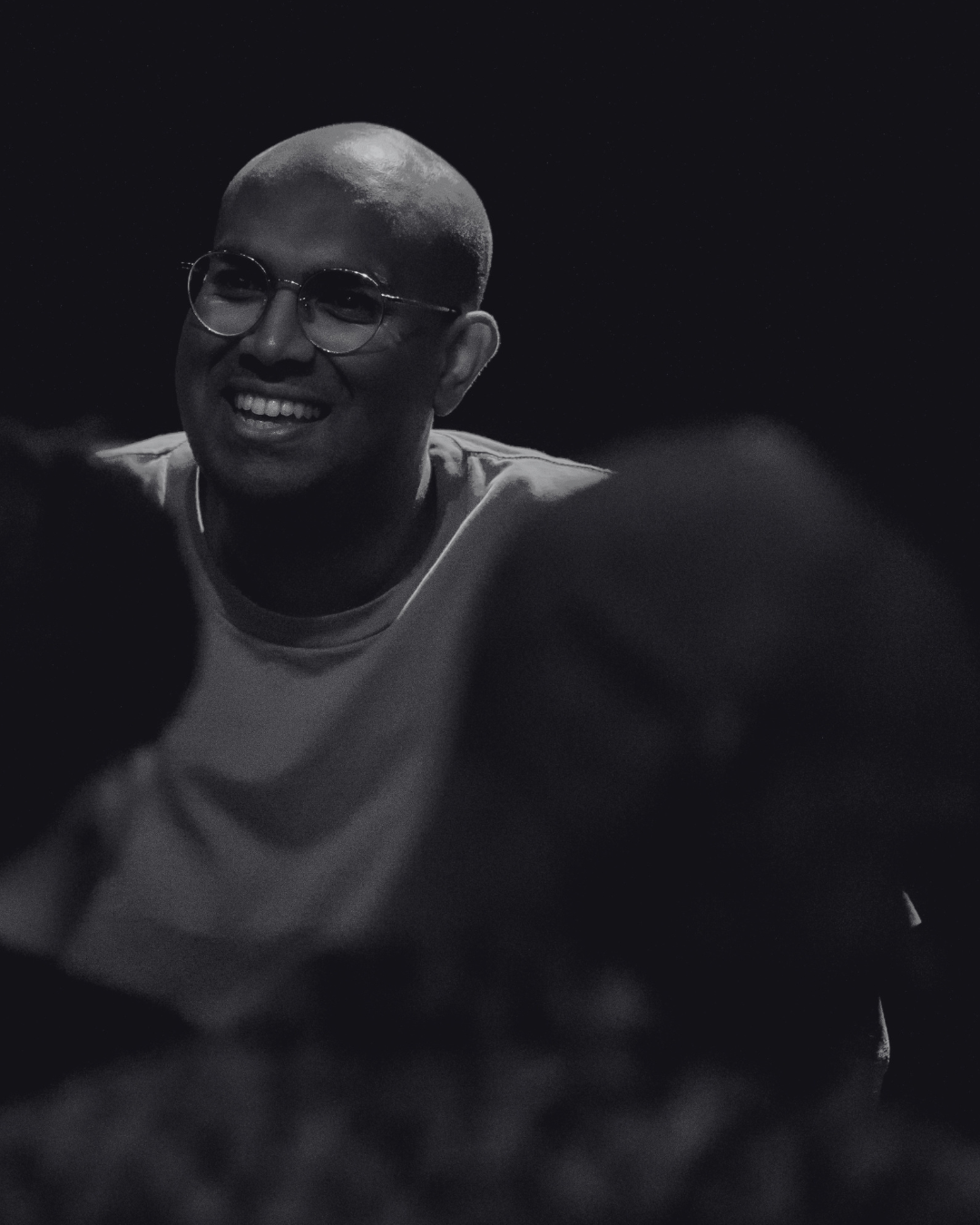 Rowan Thambar in a black and white photo, wearing a light-colored shirt, against a dark background.