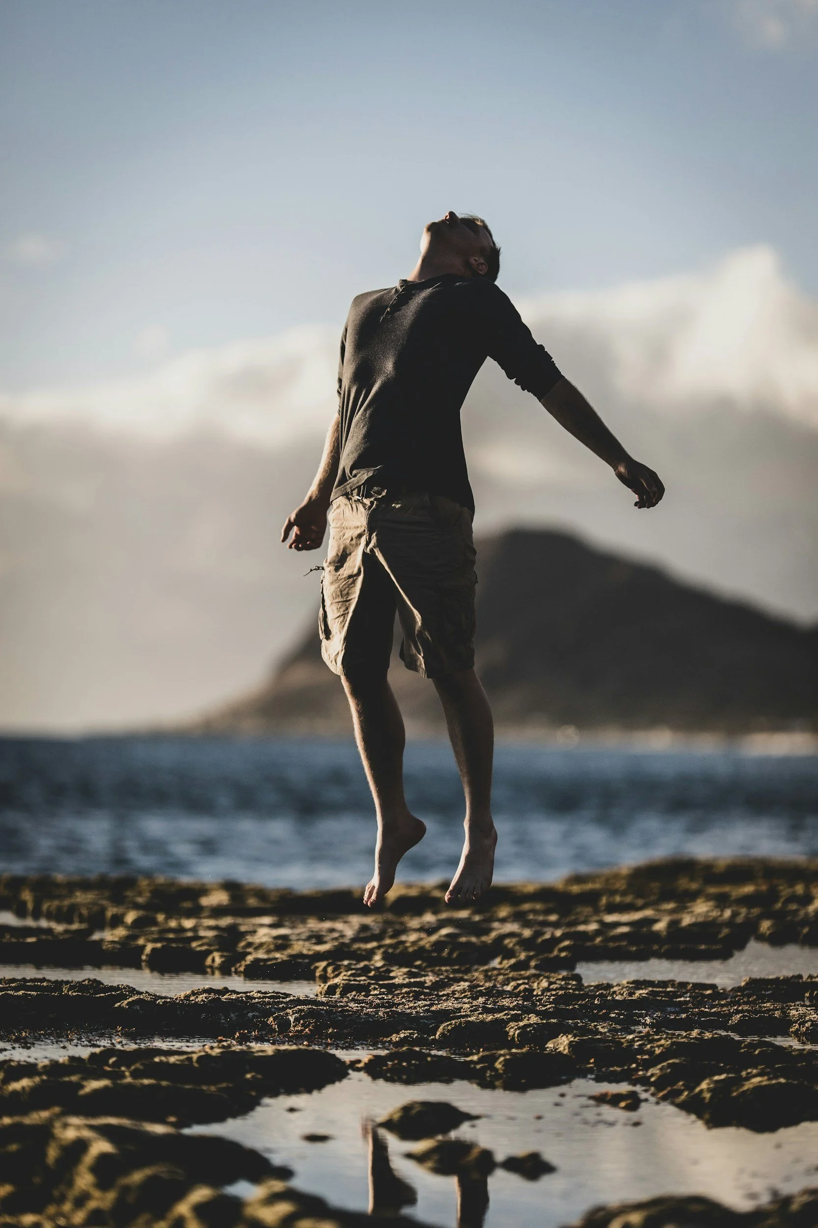 A person jumping on a beach with a body of water and cloudy sky in the background.