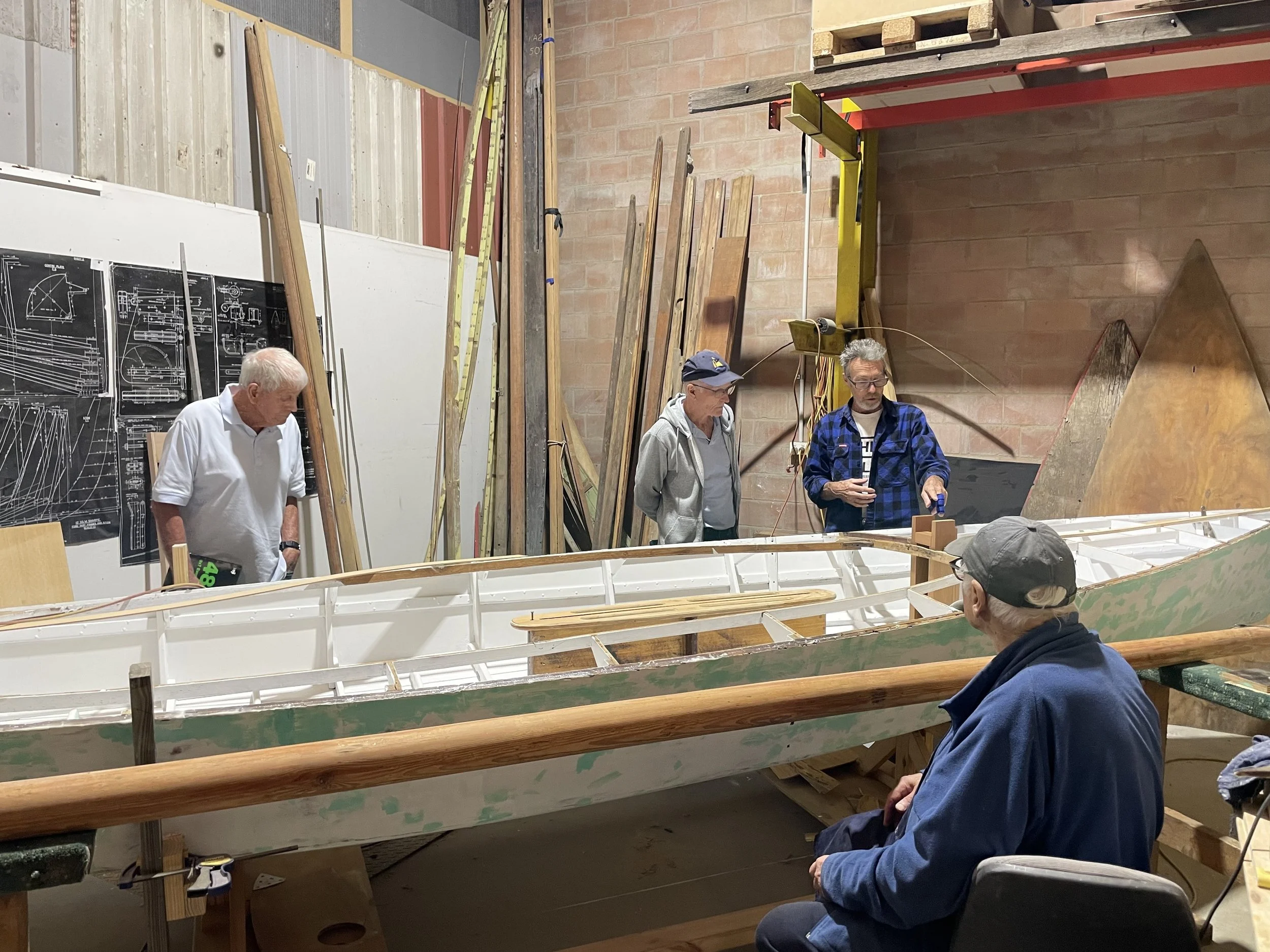 'Falcon III' undergoing renovation in the Swan River Sailing Dinghy Heritage Association workshop. The vessel blueprints are on the wall.