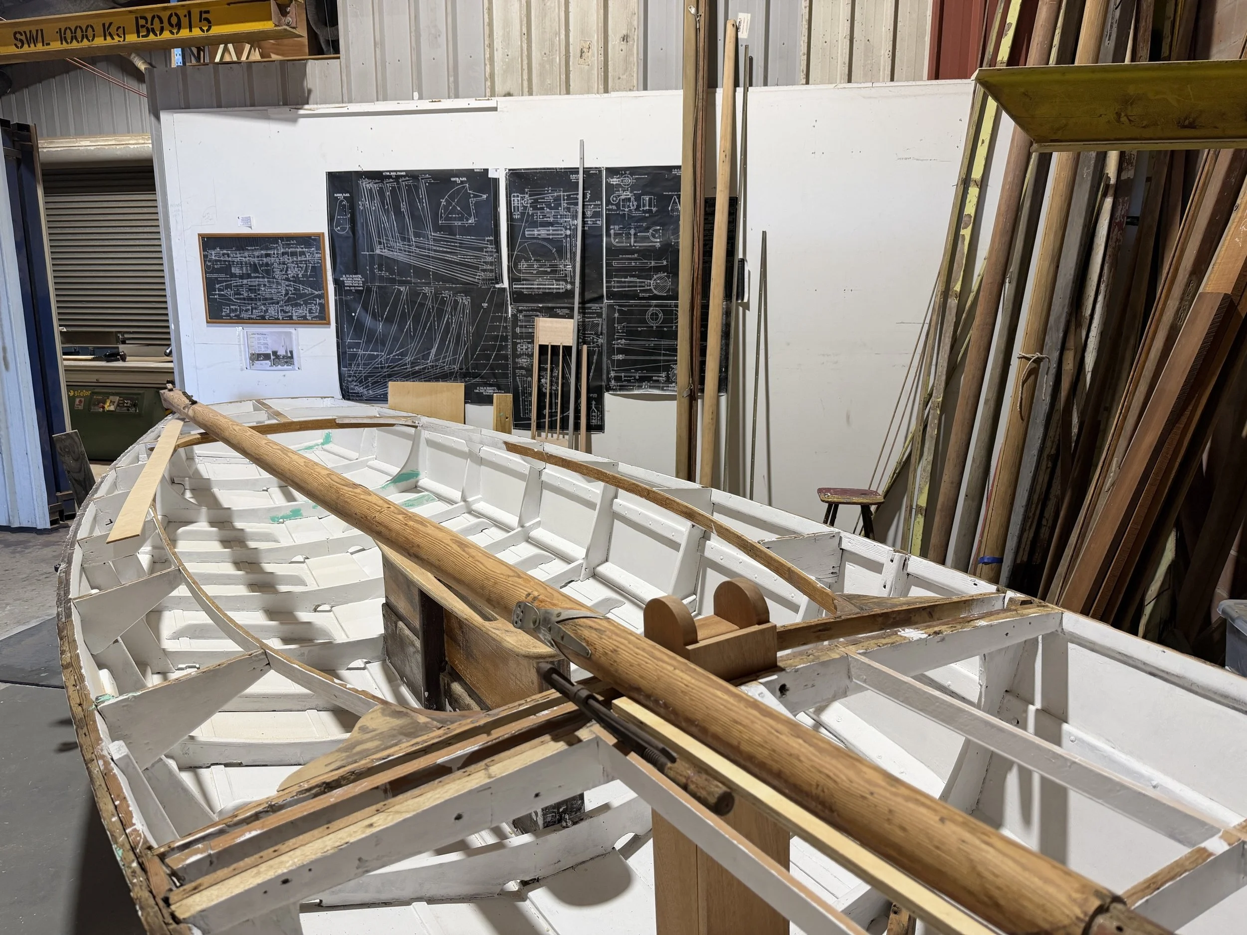 Falcon III under renovation, blueprints on the wall at the Swan River Sailing Dinghy Heritage Association.
