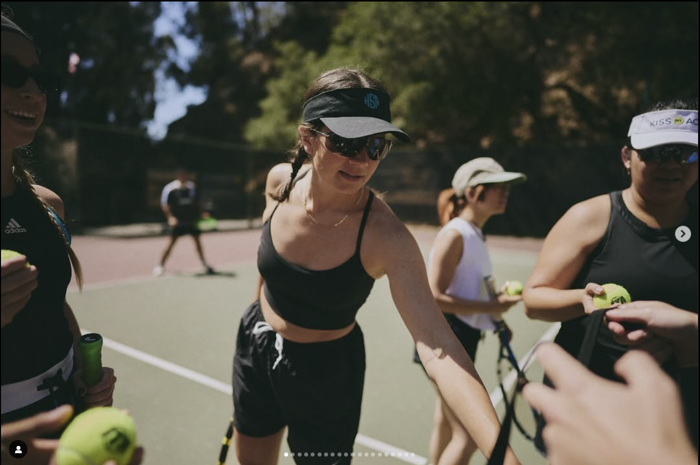 A group of women in sportswear holding tennis balls on a tennis court.