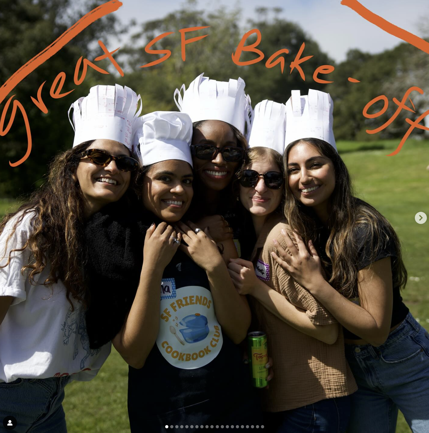 Group of five women standing outdoors, wearing chef hats with notes and sunglasses, smiling and hugging, in a park or garden setting.