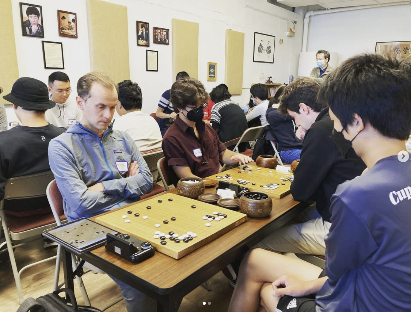People playing the game Go at a tournament, with spectators watching in the background.