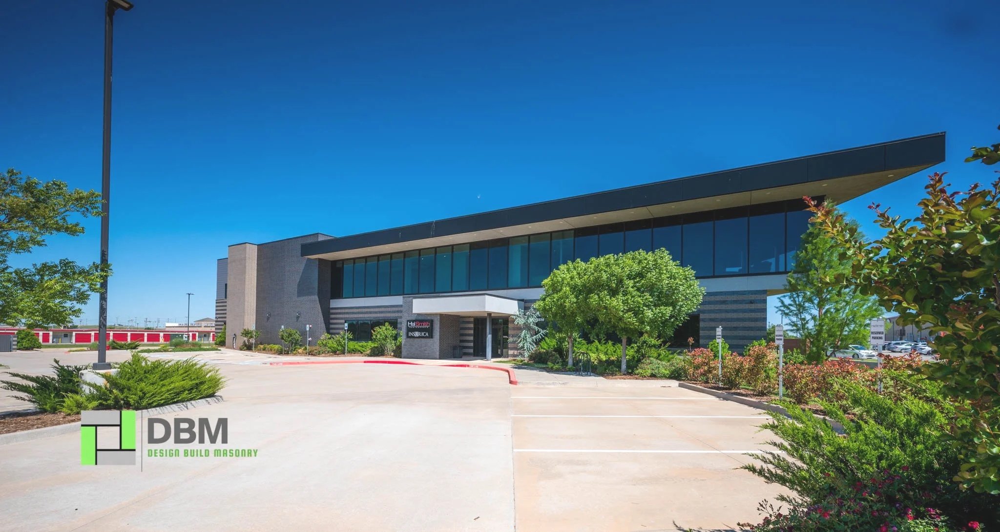 Modern office building with glass windows and landscaped parking lot under a clear blue sky.