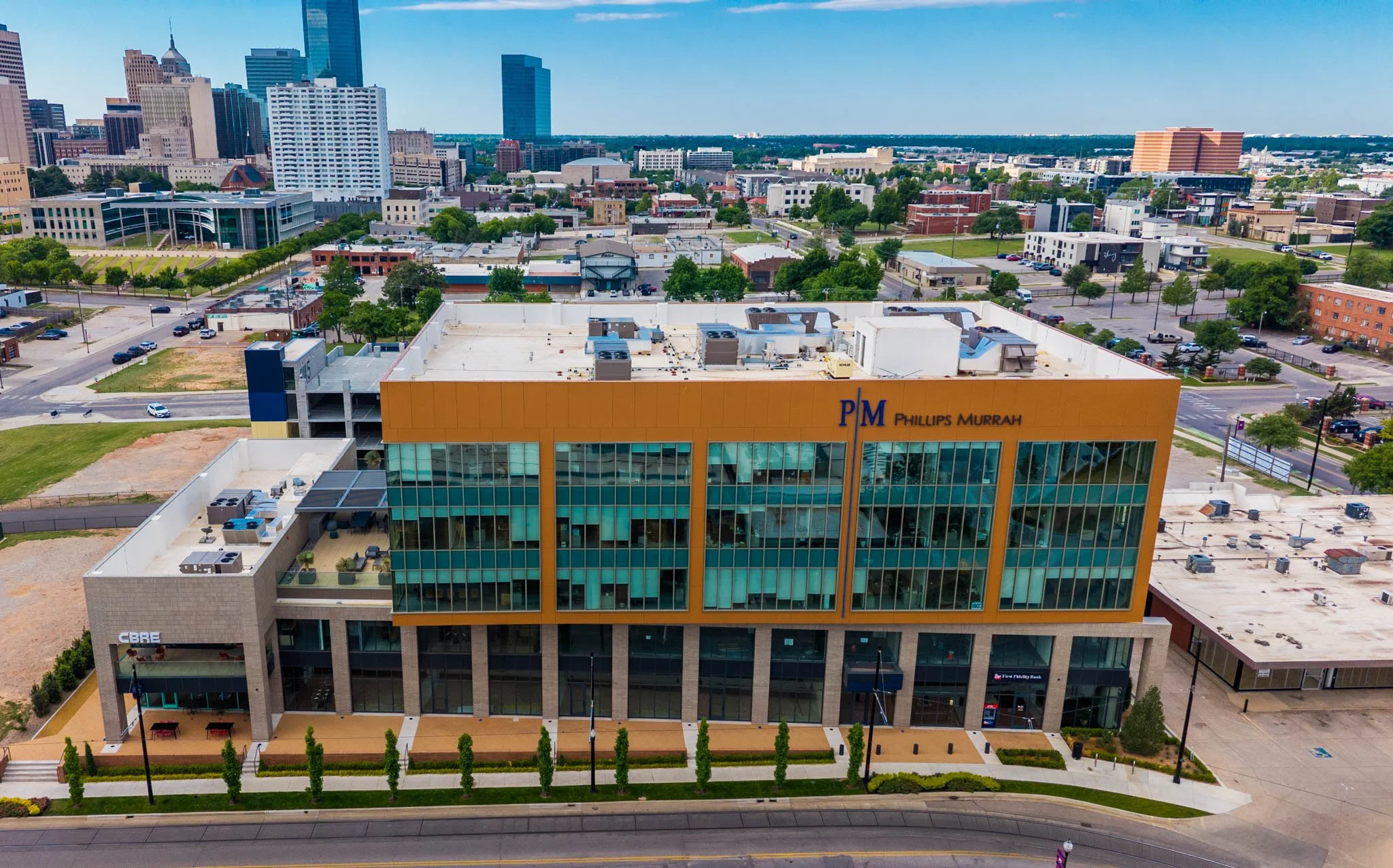 Aerial view of a city skyline with tall buildings, a parking lot, and a parking garage with a sign for Phillips Murrah law firm in the foreground.