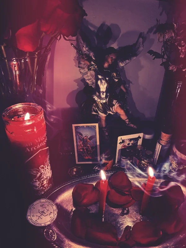 A shrine with lit candles, roses, and spiritual items, including two tarot cards set against a dark background.