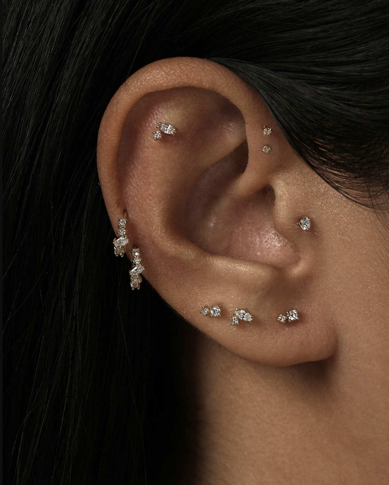 Close-up of a human ear adorned with multiple small diamond earrings in various piercing locations.