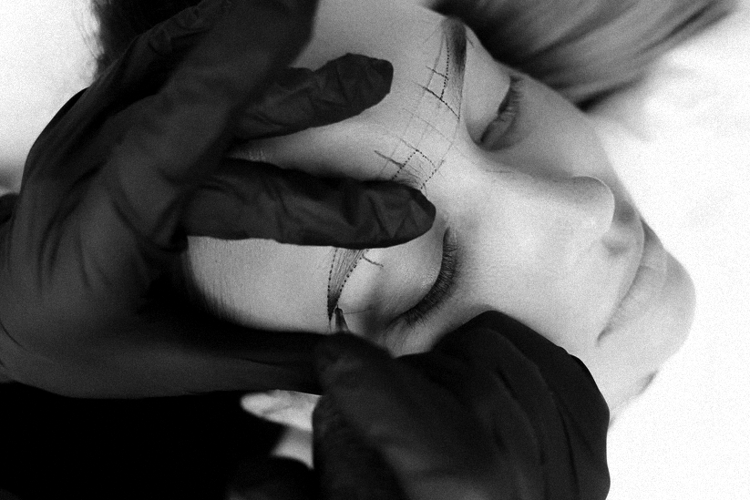 Close-up of a person receiving a cosmetic or eyelash tattooing procedure, with a tattoo artist using gloves and a fine needle near closed eyes.