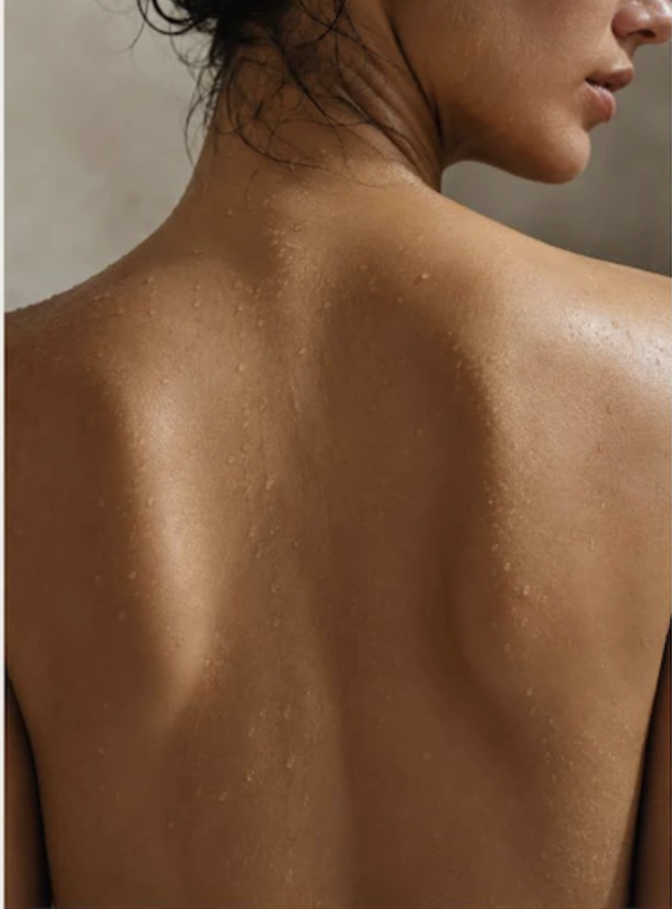 Close-up of a woman's back, showing her shoulder blades and skin with water droplets.