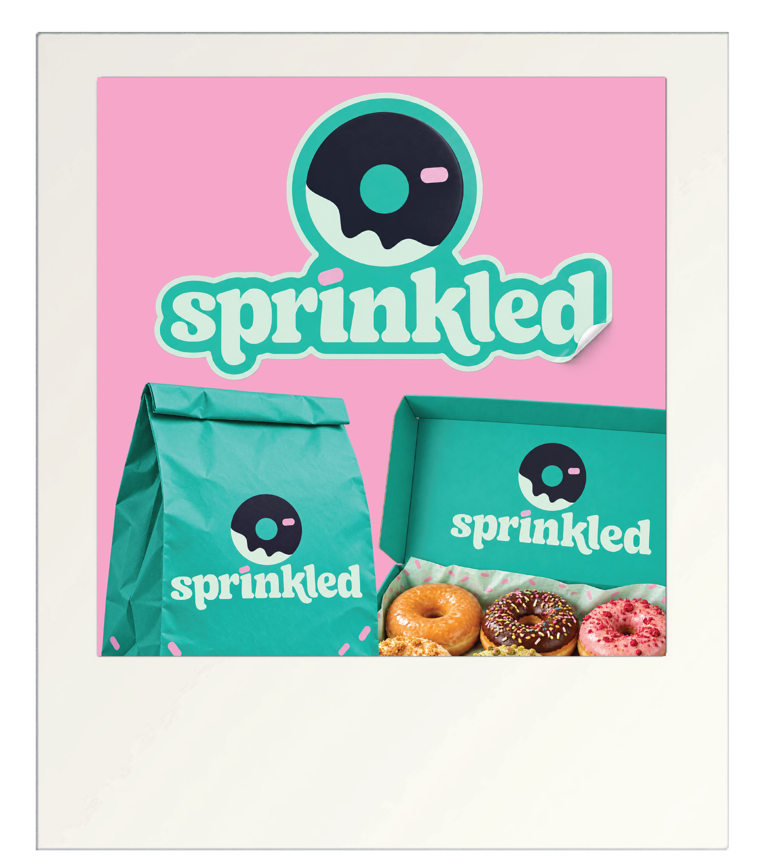 A box of assorted donuts with colorful icing and sprinkles, placed in front of a pink poster with a logo and the word 'sprinkled' on it.
