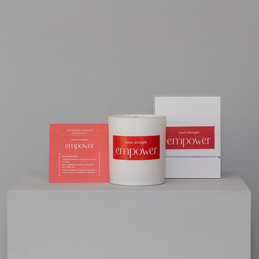 A white jar with a red label and white lid, a red box, and a white box with red accents, displayed on a gray surface against a gray background.