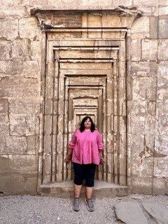 A woman standing in front of a stone wall with multiple rectangular archways.