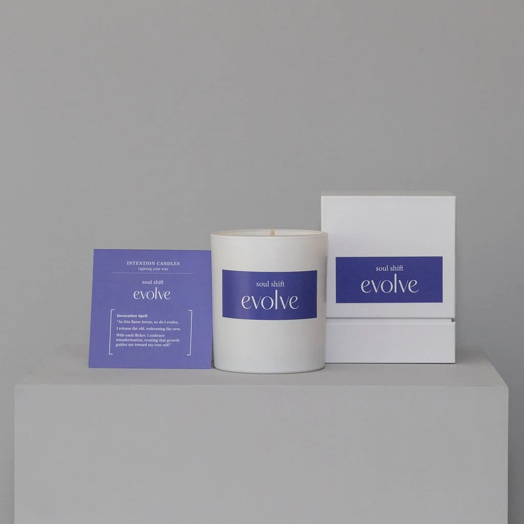 A white jar and box with blue and white labels, and a small purple packet, all on a gray surface against a gray background.