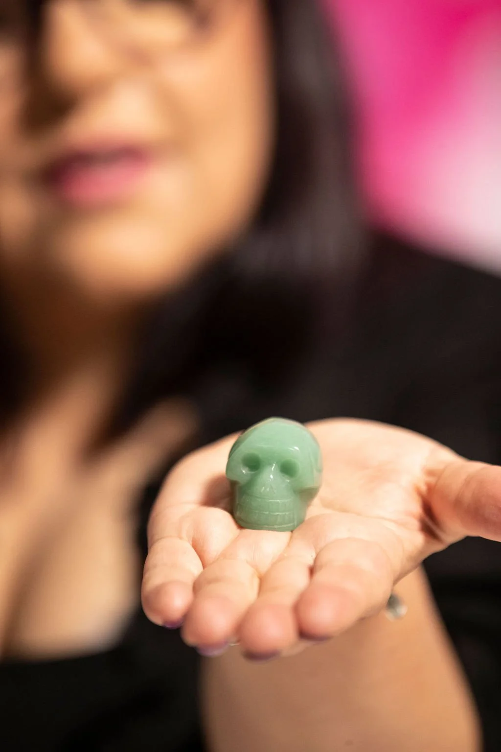 Person holding a small green skull-shaped object made of jade or similar material.