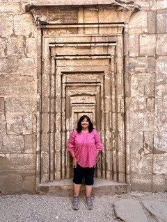 Woman standing in front of an ancient stone doorway with multiple nested arches.