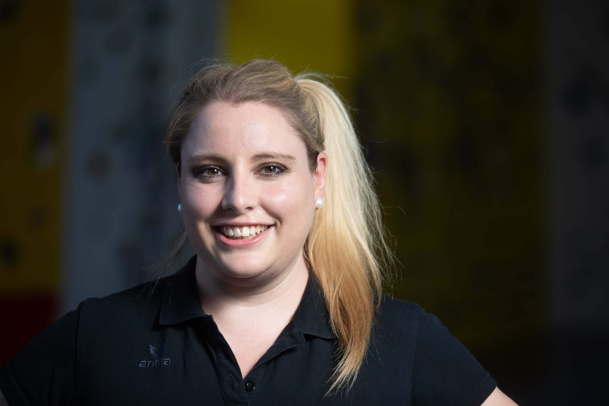 lächelnde Frau mit blonden, zusammengebundenen Haaren und einem schwarzen Poloshirt