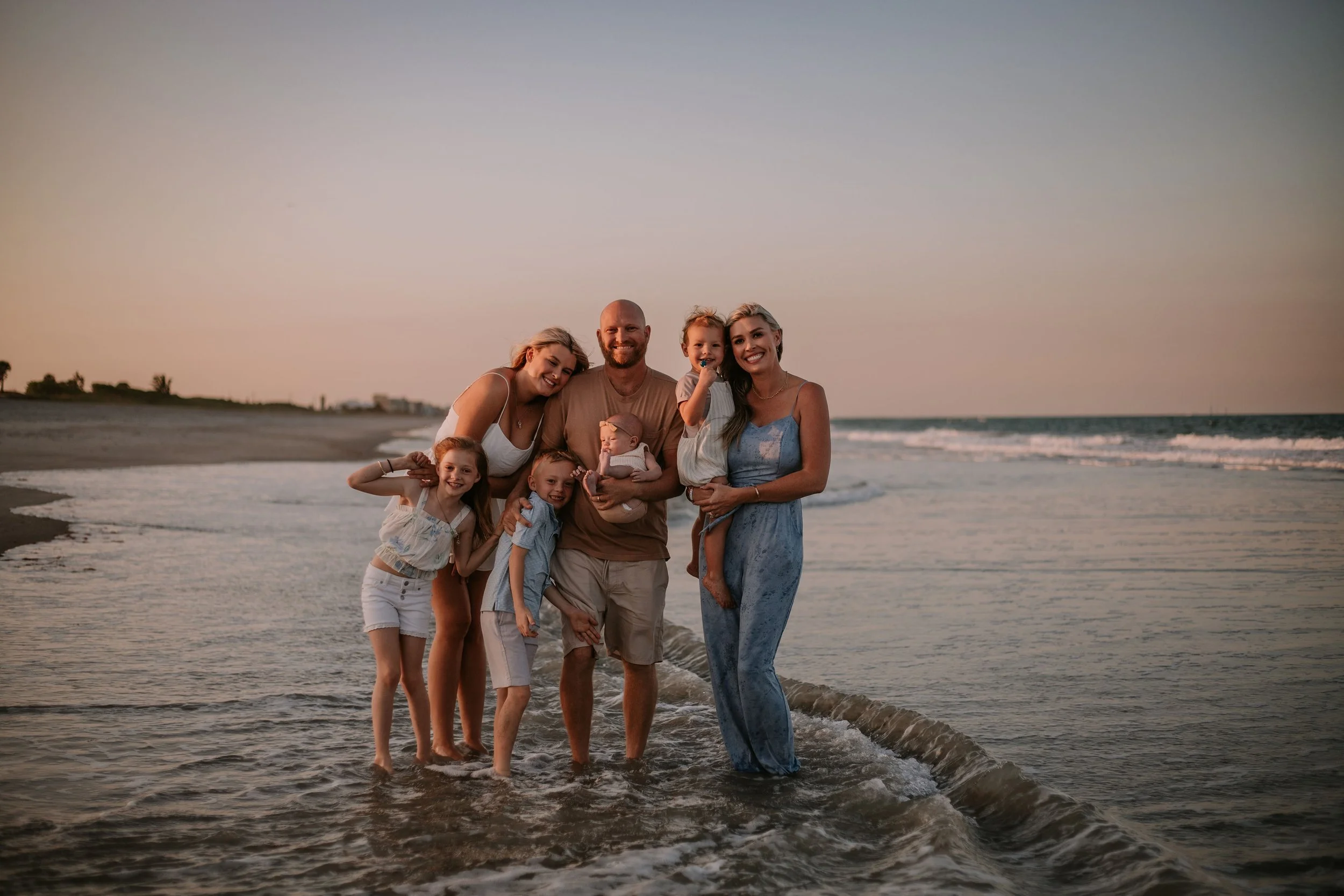 Family standing together at the beach at sunset.