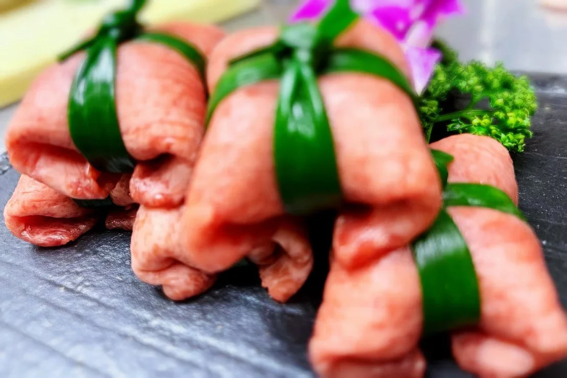 綺麗に巻かれた生肉に緑色の葉で包んだ肉の盛り合わせ