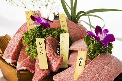 高級和牛の刺身盛り合わせ、花と葉の飾り付き、タグには肉の部位名が書かれている。
