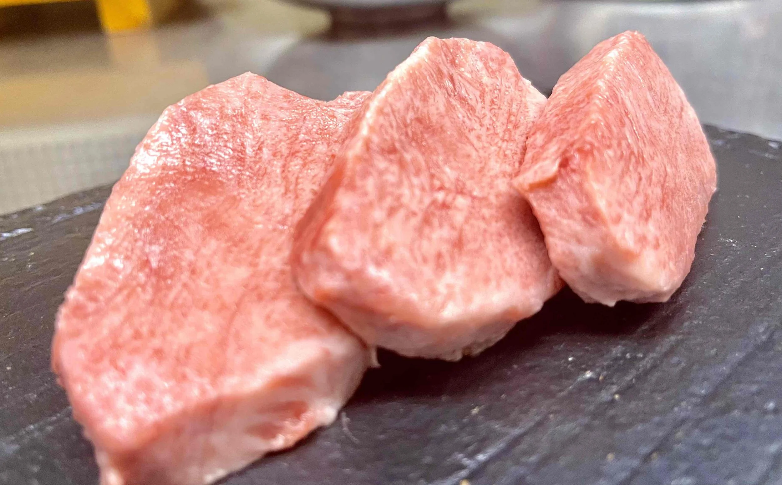 厚切りの赤身肉の塊肉。肉はピンク色で脂肪は少ない。黒い板の上に置かれている。
