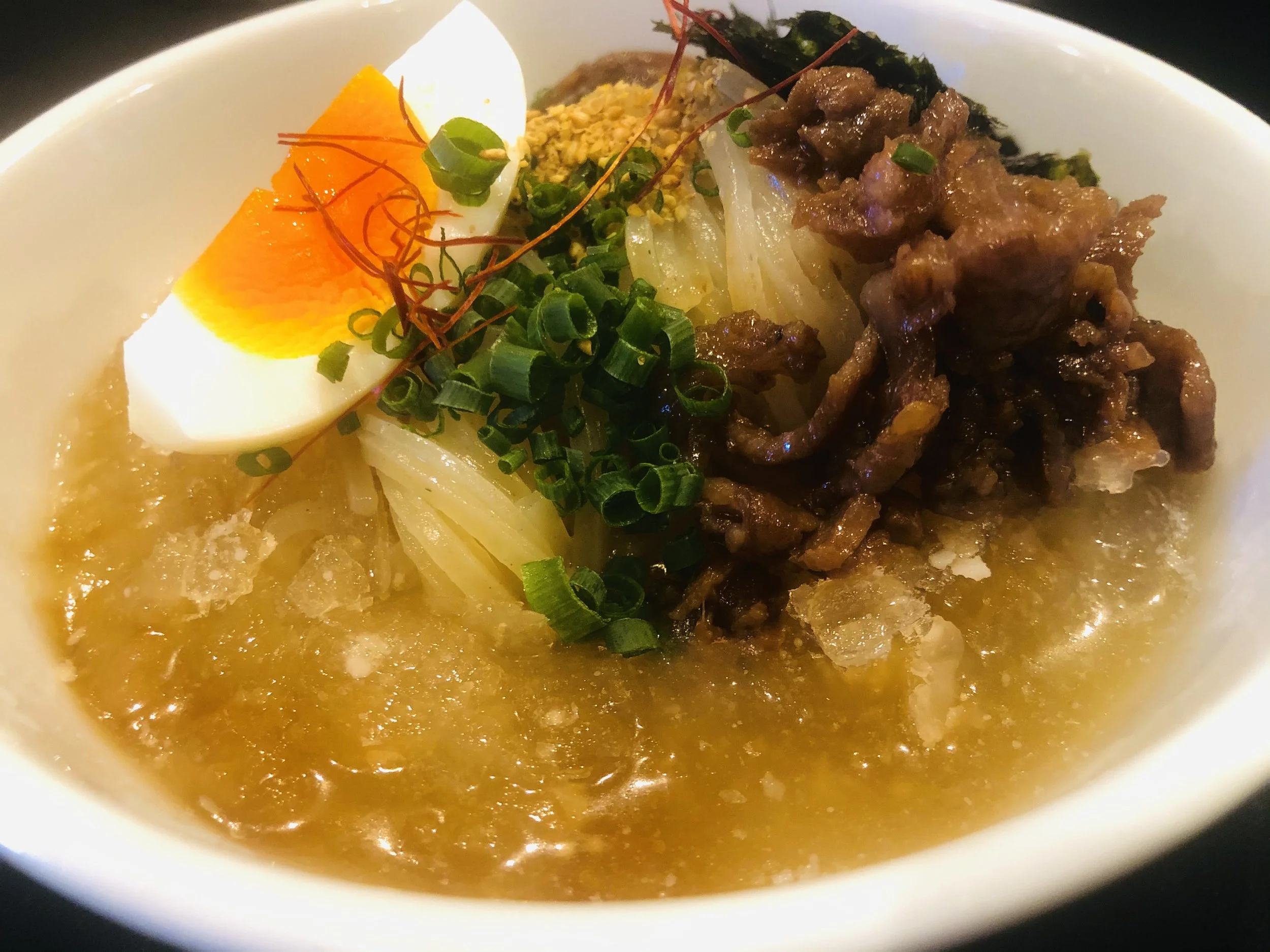 卵、緑のネギ、肉、ナッツ、海藻、レッドペッパーなどの様々なトッピングが載った料理のアップ。