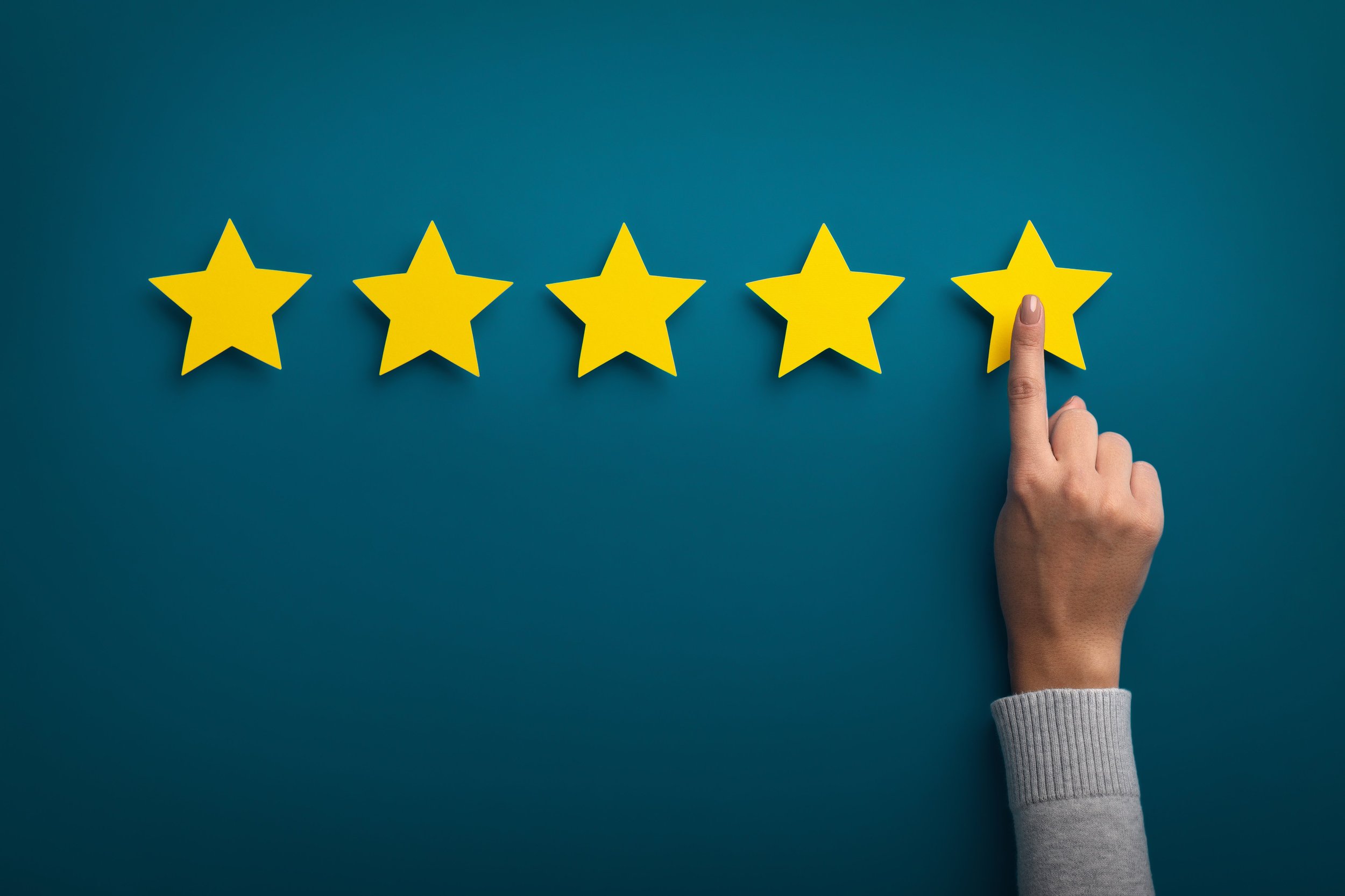 A hand with a gray sleeve touching a yellow star on a row of five yellow stars, symbolizing a five-star rating, against a blue background.