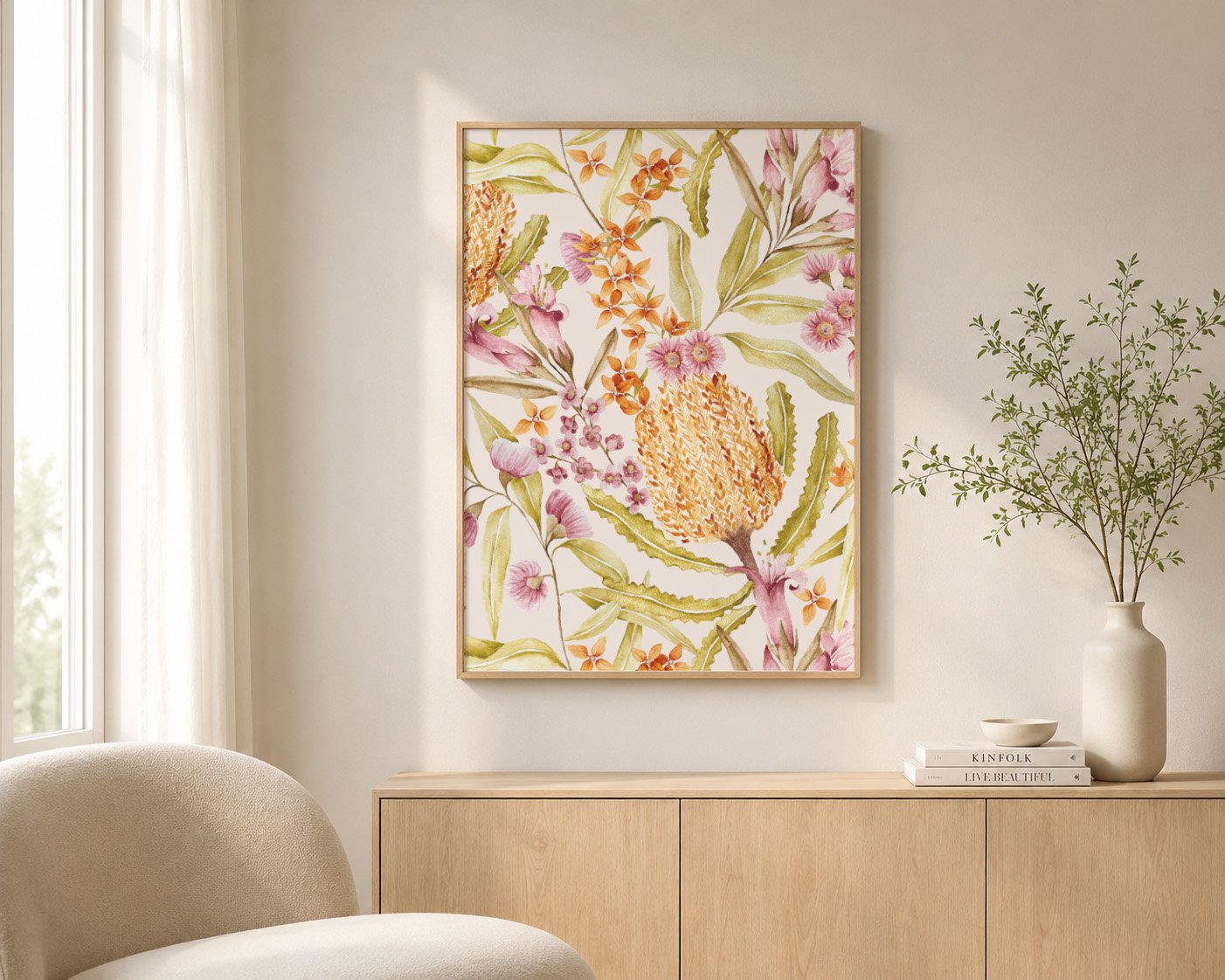 Interior of a modern living space with a light wooden sideboard, a large botanical framed artwork, a white vase with greenery, and a neutral-colored chair near a window with sheer curtains.