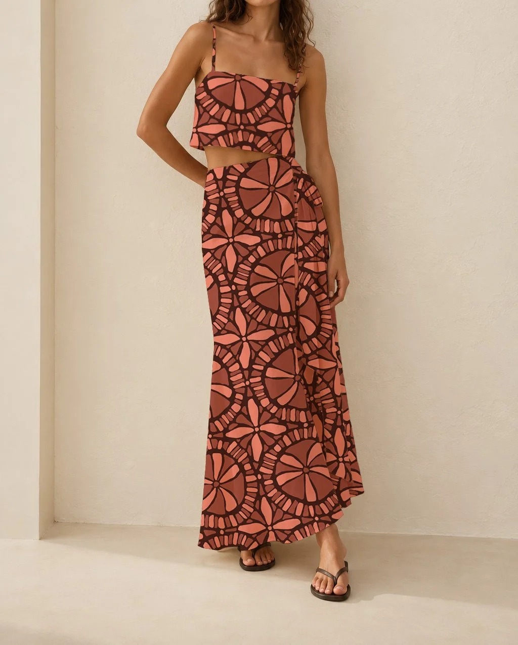 A woman wearing a matching two-piece skirt and crop top set with a geometric, flower-like pattern in shades of pink and dark brown.