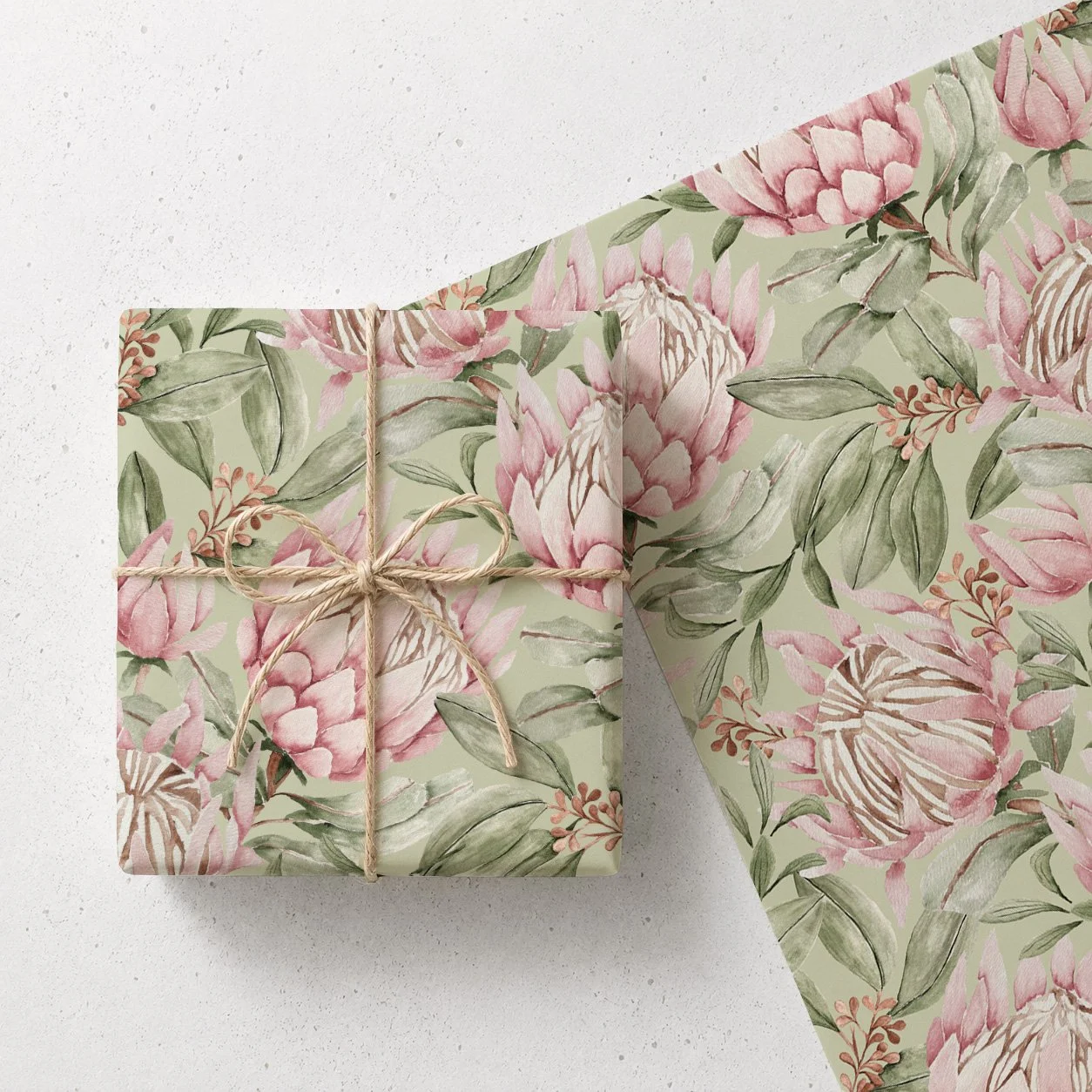 A gift wrapped in floral patterned paper with pink flowers and green leaves, tied with a beige twine bow, and an empty sheet of the same paper partially unrolled nearby.