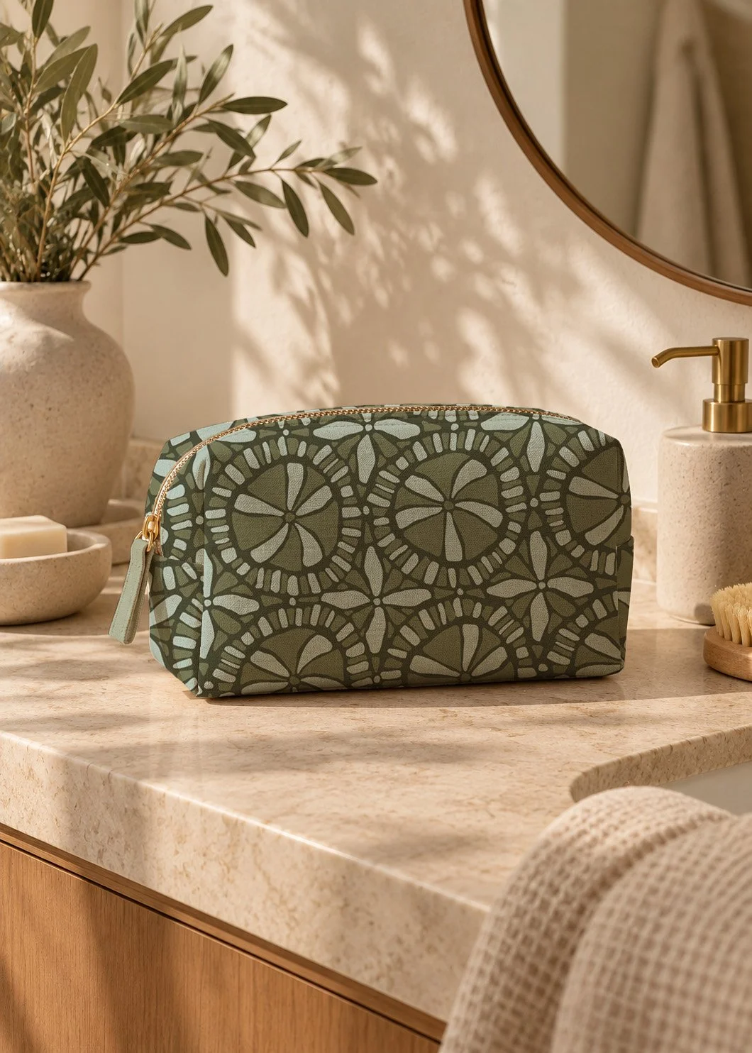A green patterned zippered pouch on a bathroom countertop with a potted plant, soap dispenser, and a circular mirror in the background.