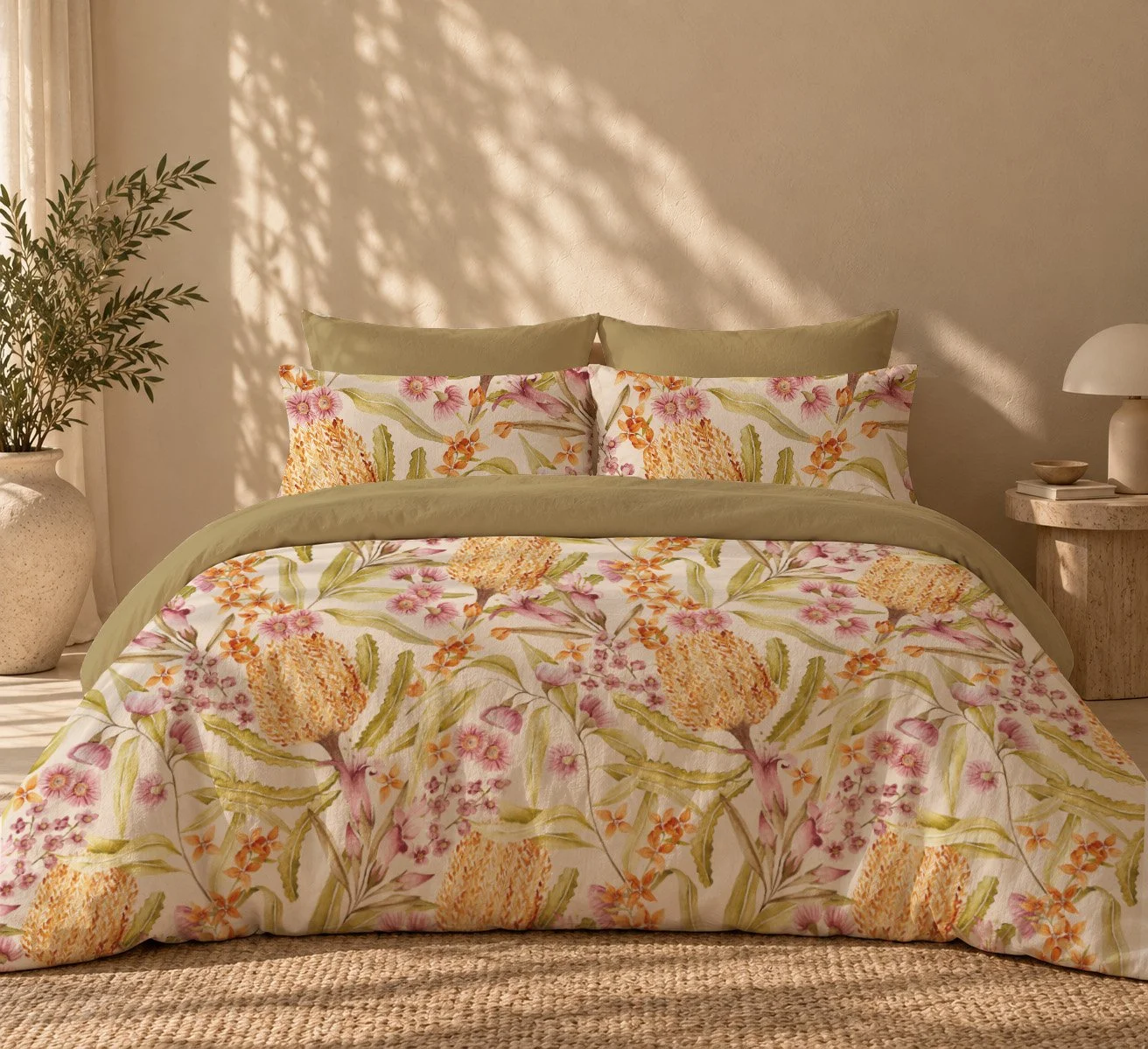 A bedroom with a bed featuring floral bedding, light green pillows, and beige walls, with a potted plant and a bedside table with a lamp.