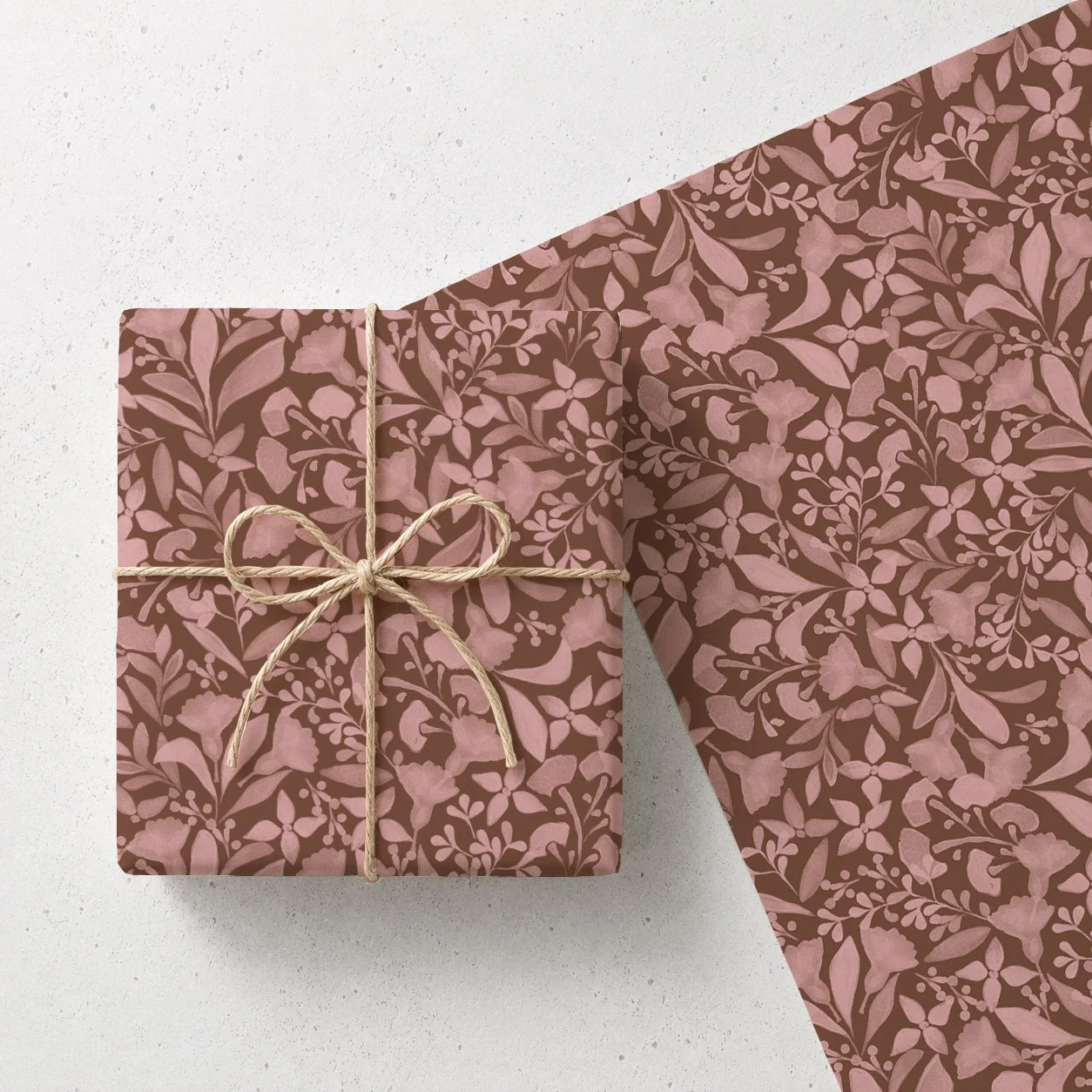 A gift wrapped in floral patterned pink and brown paper, tied with a beige string bow, with the wrapping partially open revealing more of the floral paper.