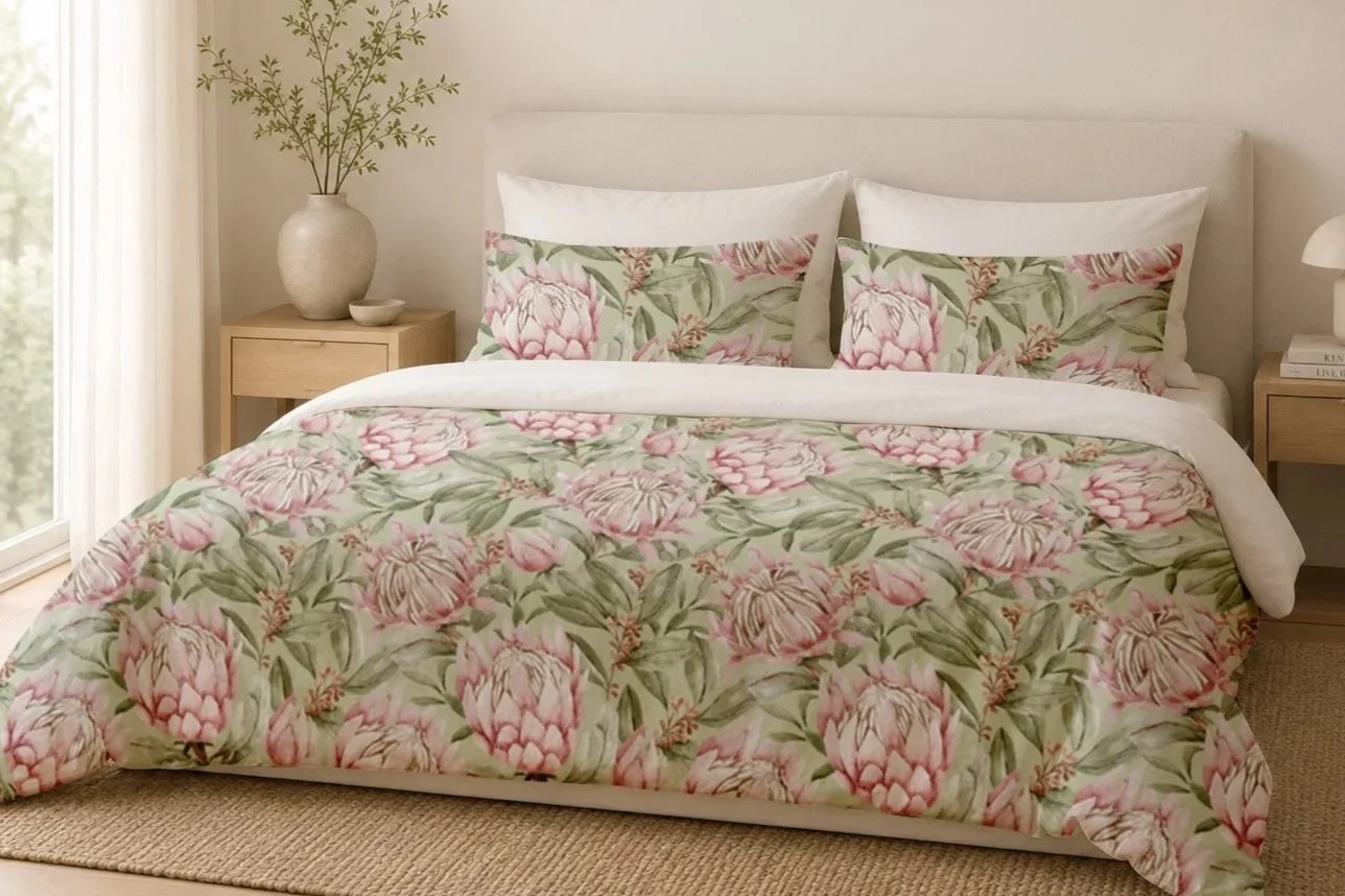 A neatly made bed with a floral comforter and matching pillows in a bright bedroom. The bed is flanked by light wooden nightstands, each with a decorative item. Natural light filters through sheer curtains on the window beside the bed.