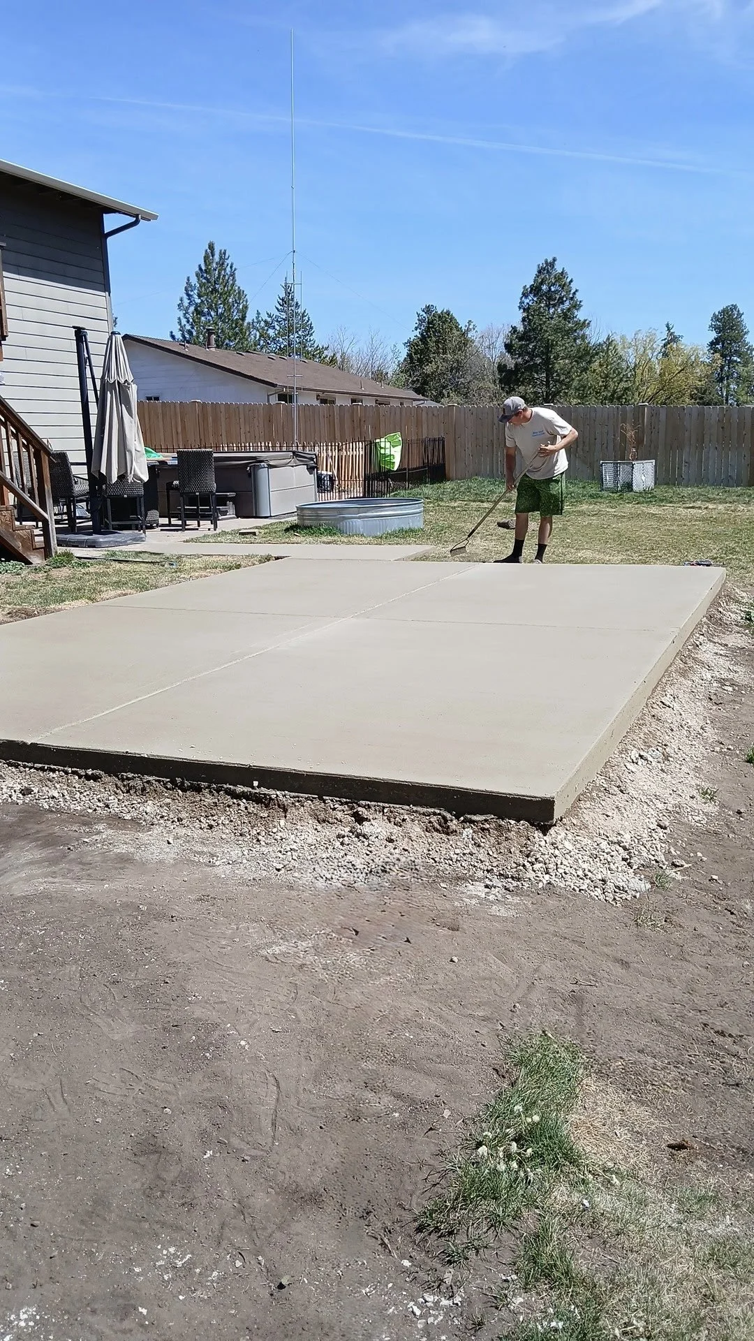 A man working on a freshly poured concrete slab in a backyard.