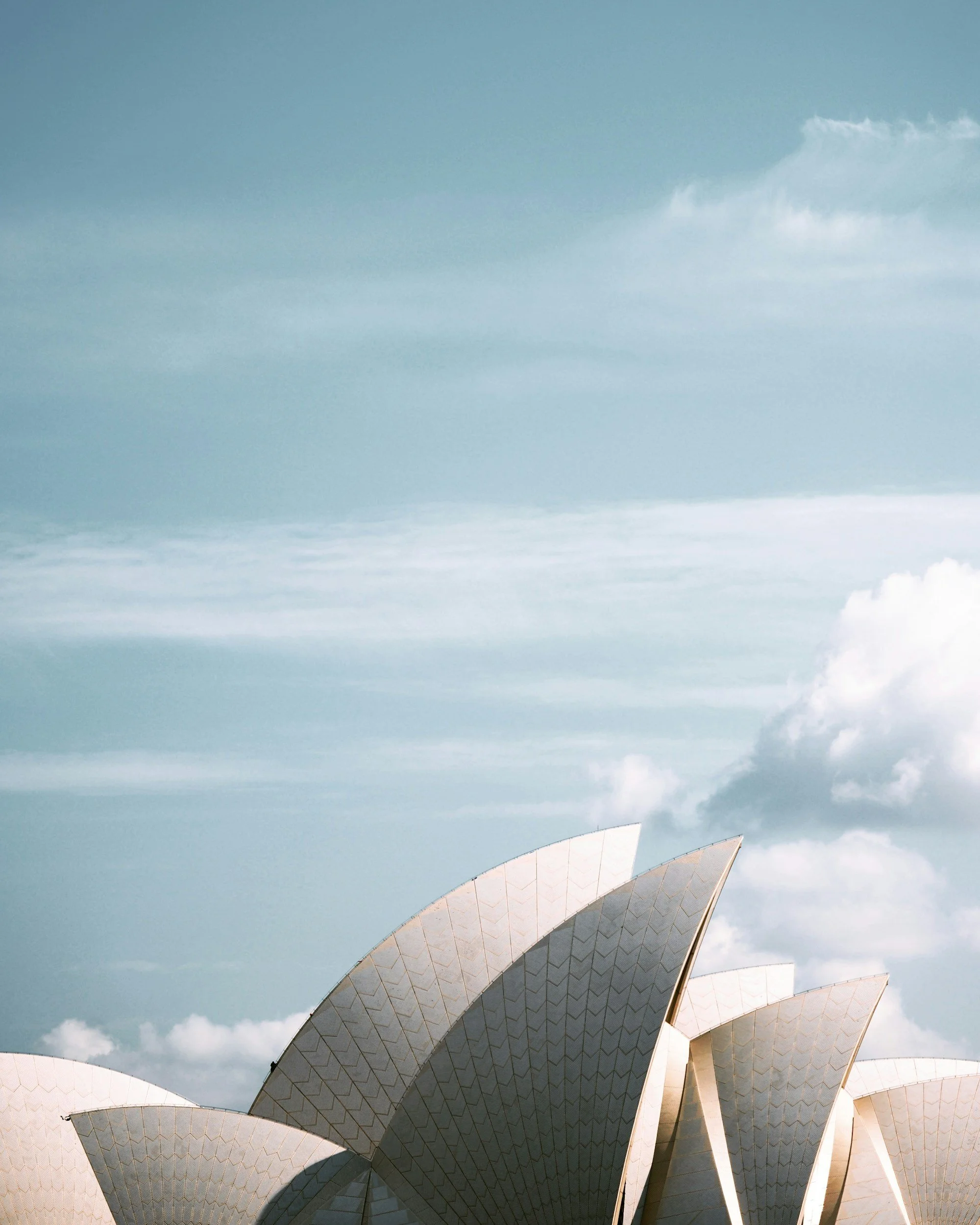 Close-up of the Sydney Opera House with its iconic sail-shaped shells, taken from a low angle against a partly cloudy sky.