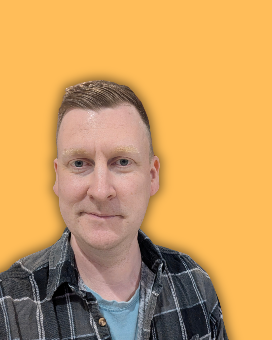 A man with short, neatly combed hair, wearing a black and gray plaid shirt over a light blue t-shirt, against an orange background.
