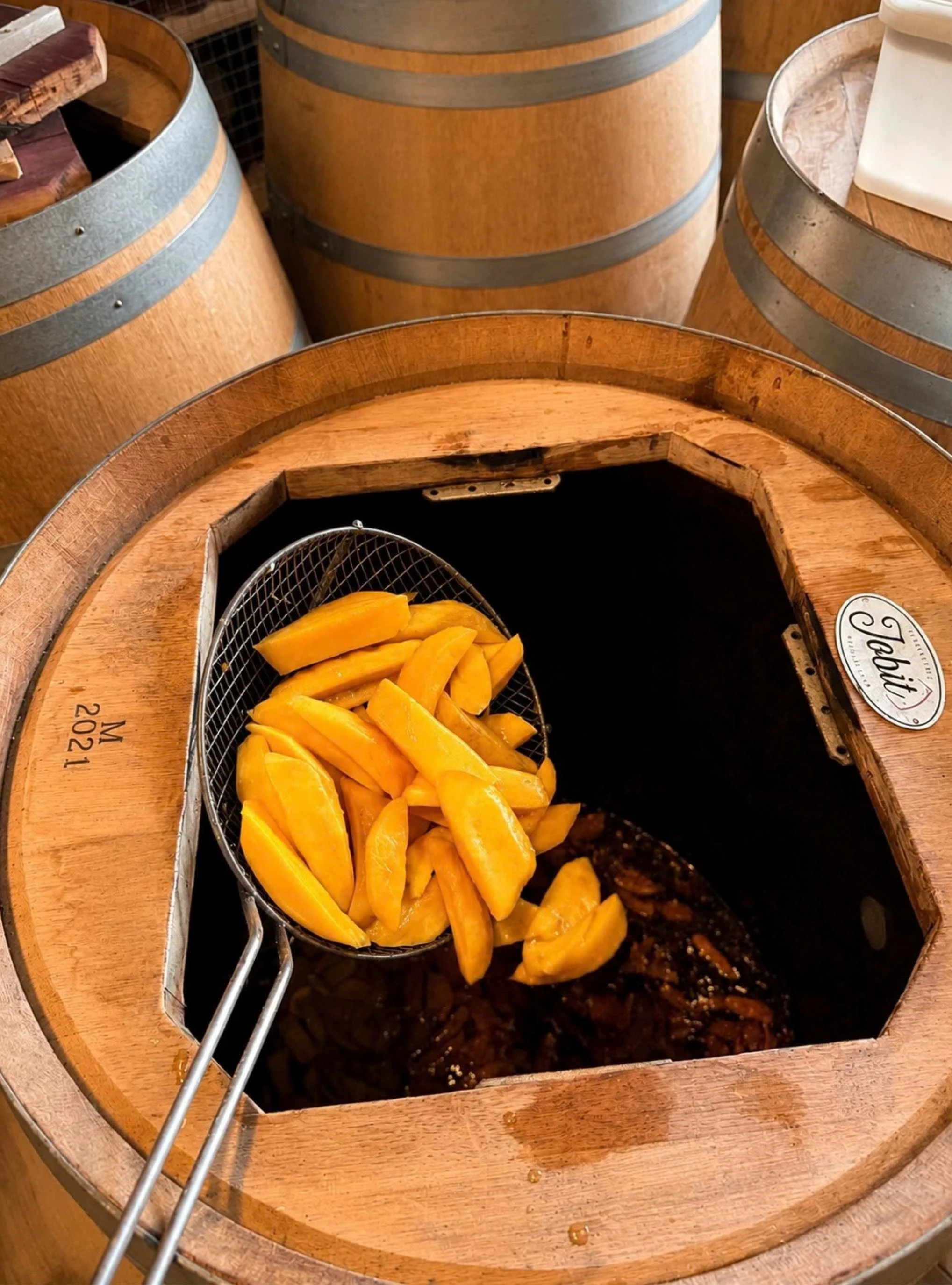 Fèves de mangue fraîches dans une passoire en métal placée sur un vieux moulin à café en bois.