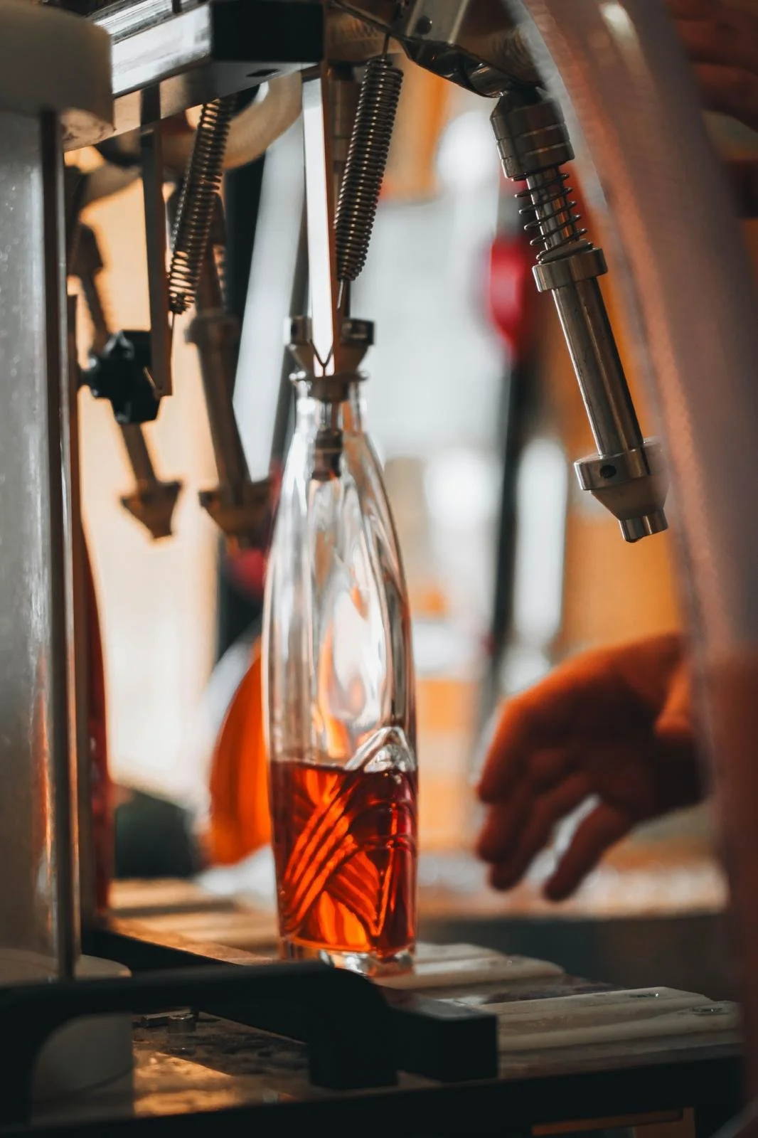 Un verre en verre avec une boisson rouge, sous une machine à soda ou à sirop. Une main est visible, probablement en train de manipuler la machine.