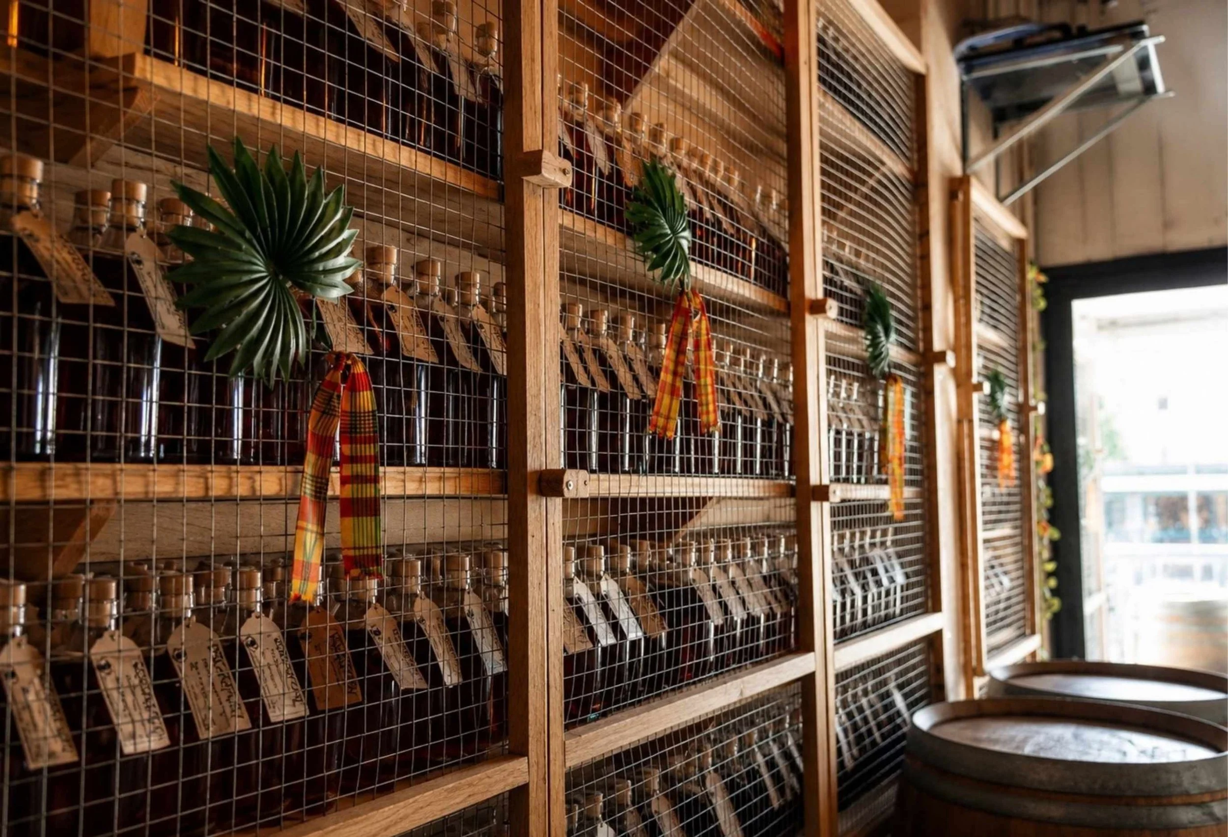 Étagères en bois avec des bocaux en verre contenant des graines ou des poudres, décorées avec des feuilles vertes et des rubans colorés, dans un intérieur lumineux.