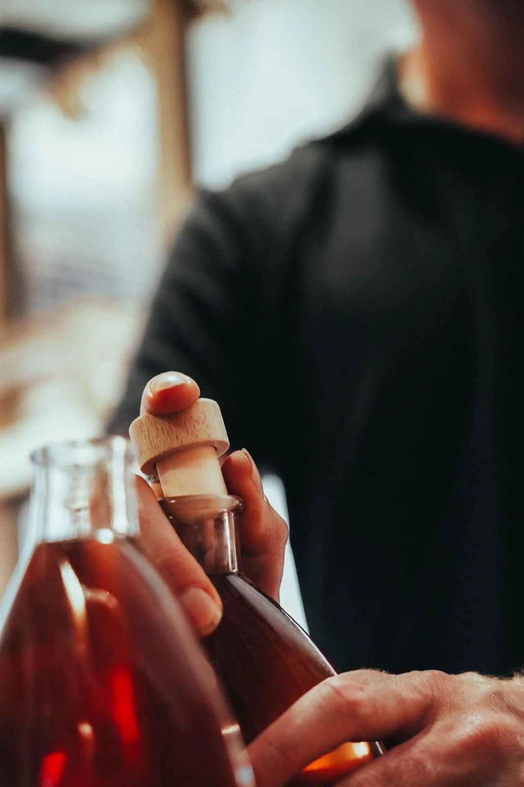 Une personne tenant une bouteille en verre avec un bouchon en bois, probablement en train de verser ou de préparer une boisson.