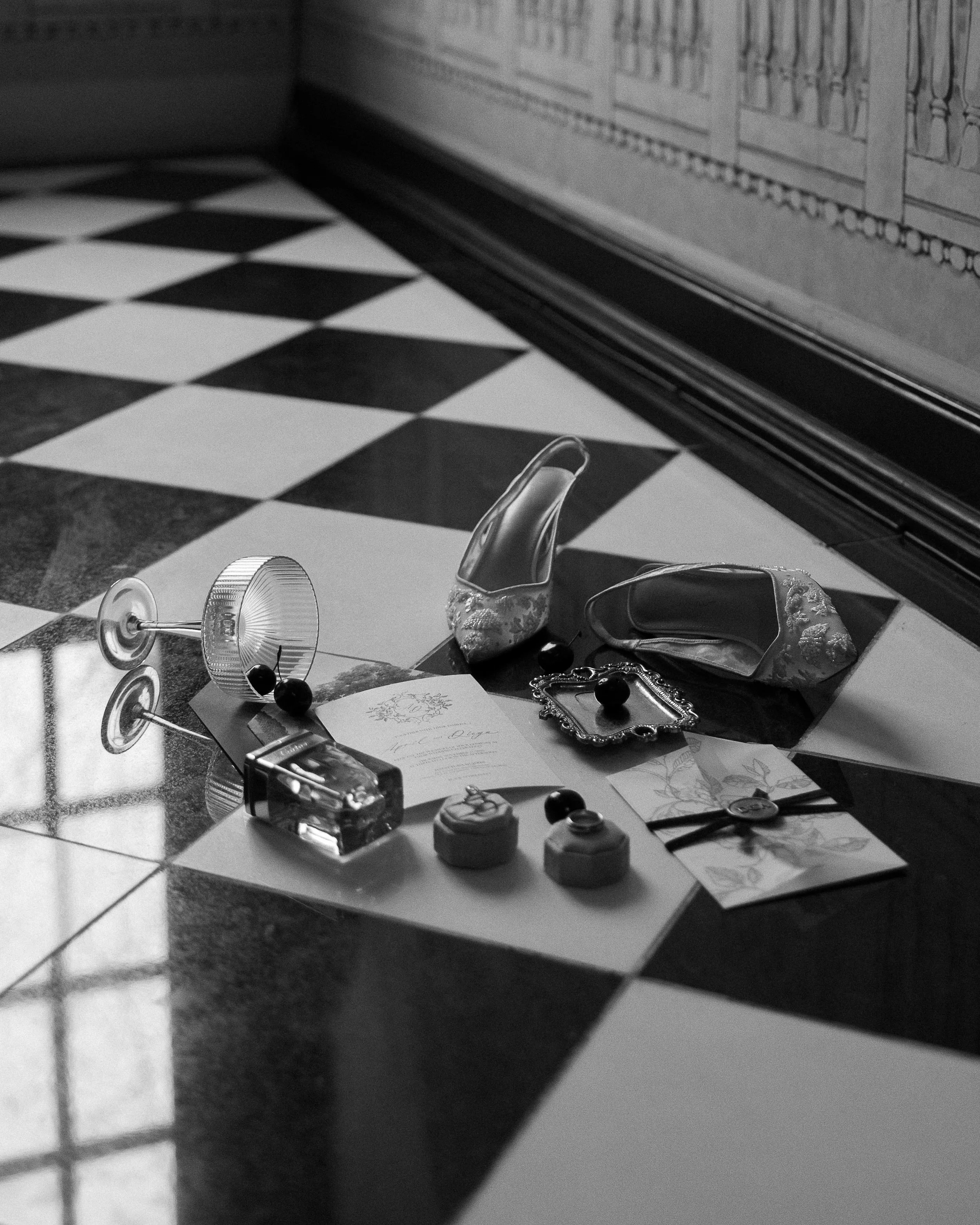 Party table with glasses, jewelry, and napkins with floral design on a black and white checkered floor, near a glass door or window.