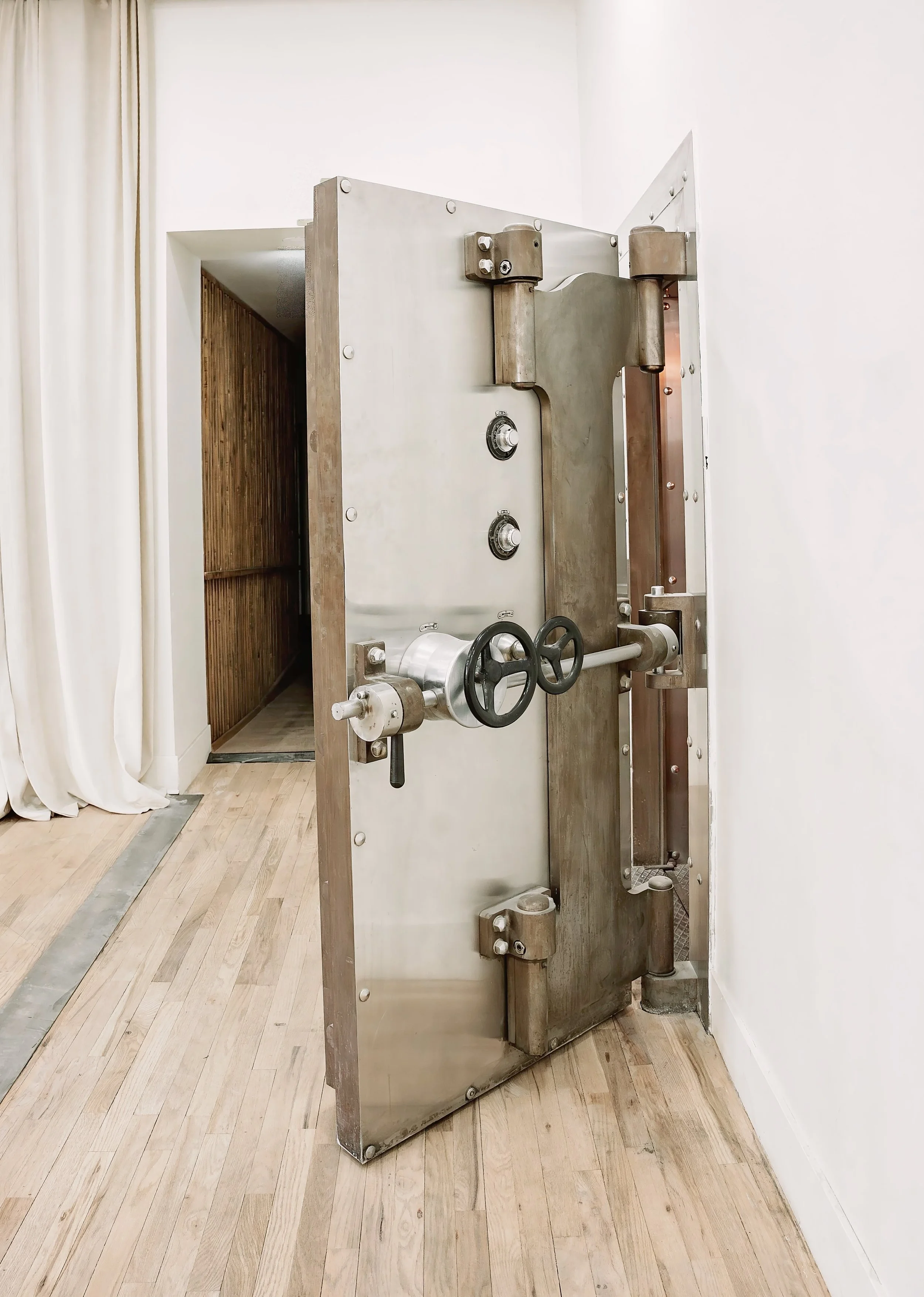 A vintage industrial machine with large circular dials and metal pipes, set in a room with wooden flooring and white walls.