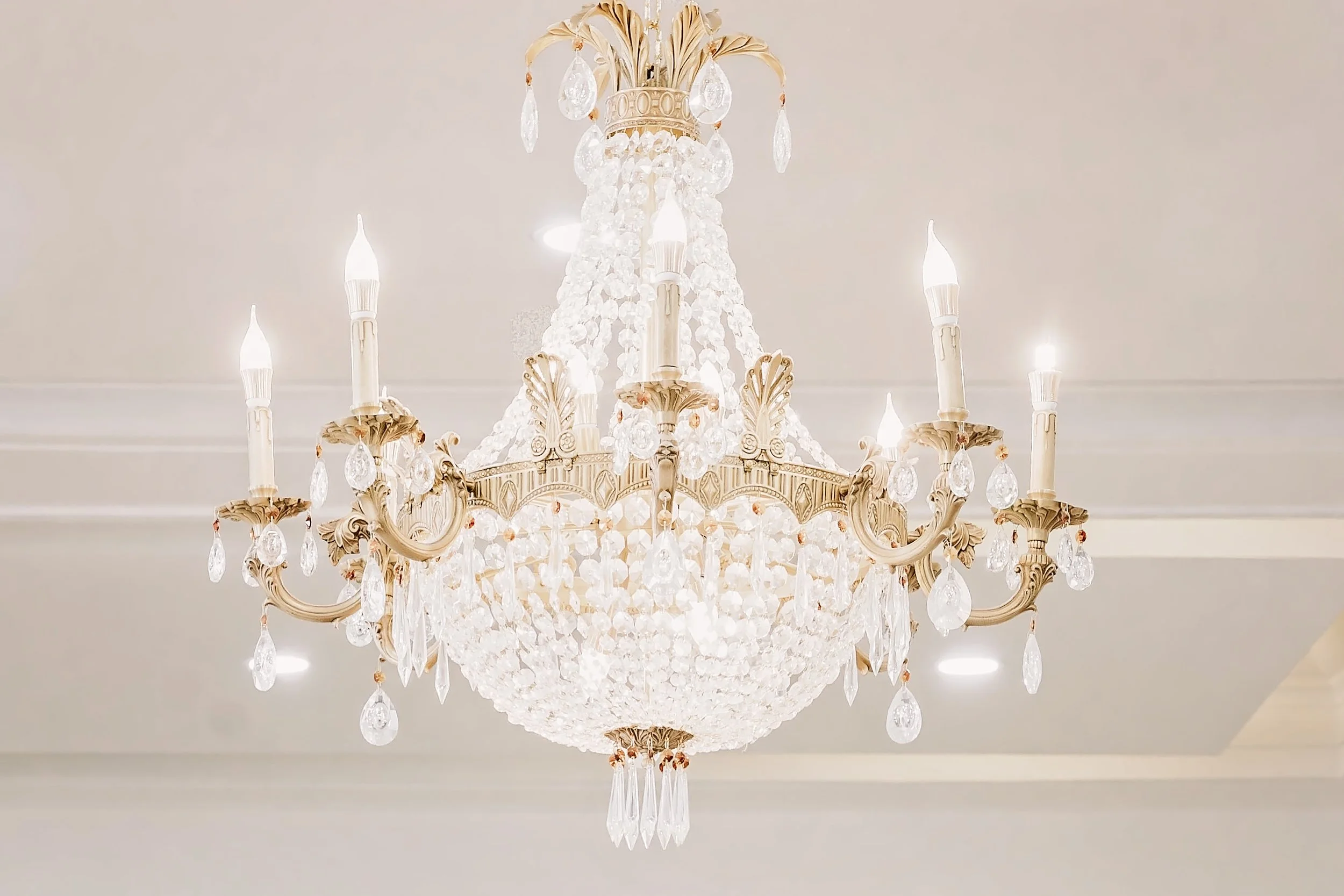 Chandelier with crystal and glass drops hanging from ornate gold and cream-colored metal frame, mounted on a white ceiling.