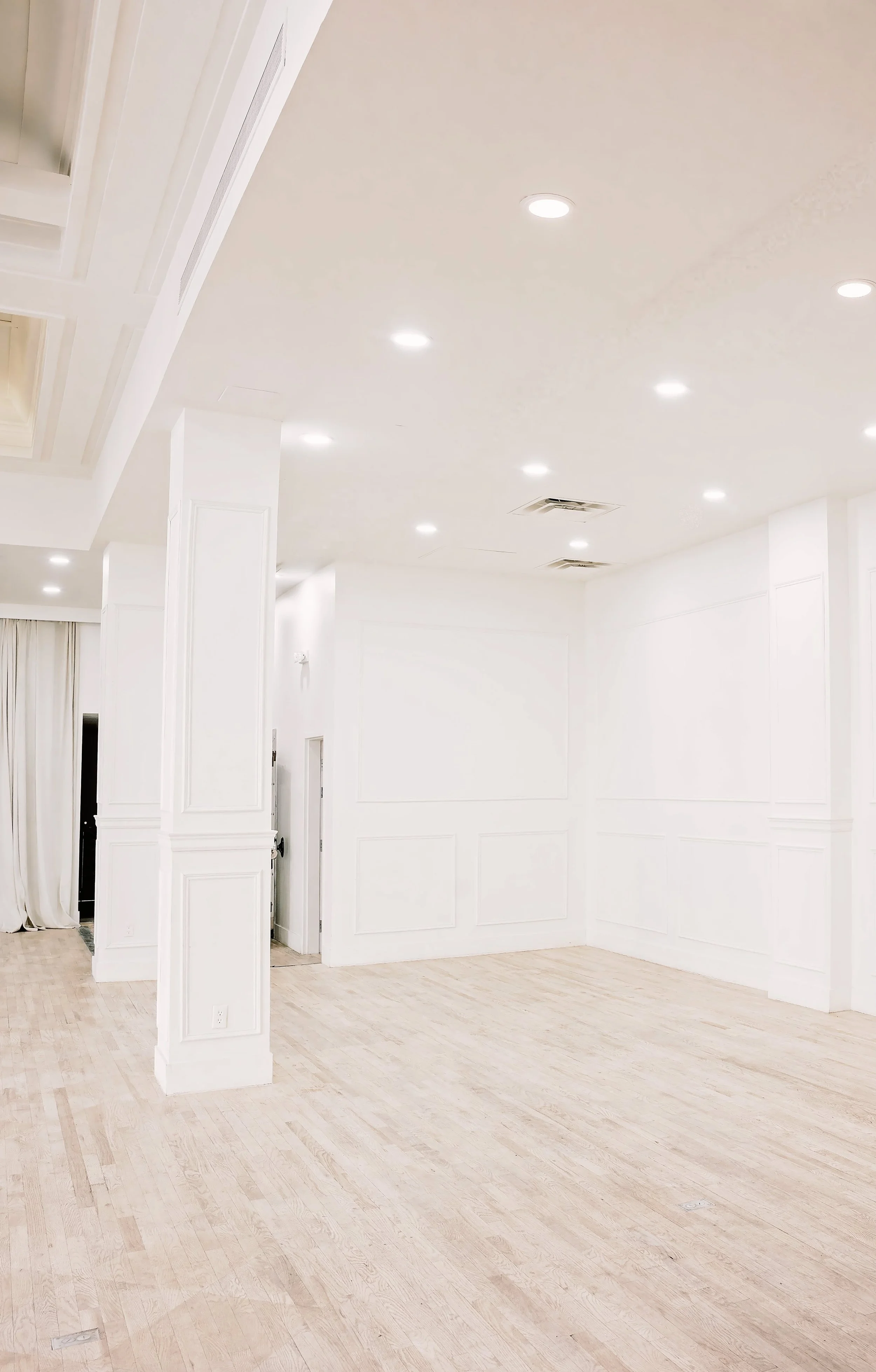 Empty room with white walls, light-colored wooden flooring, and recessed ceiling lights.