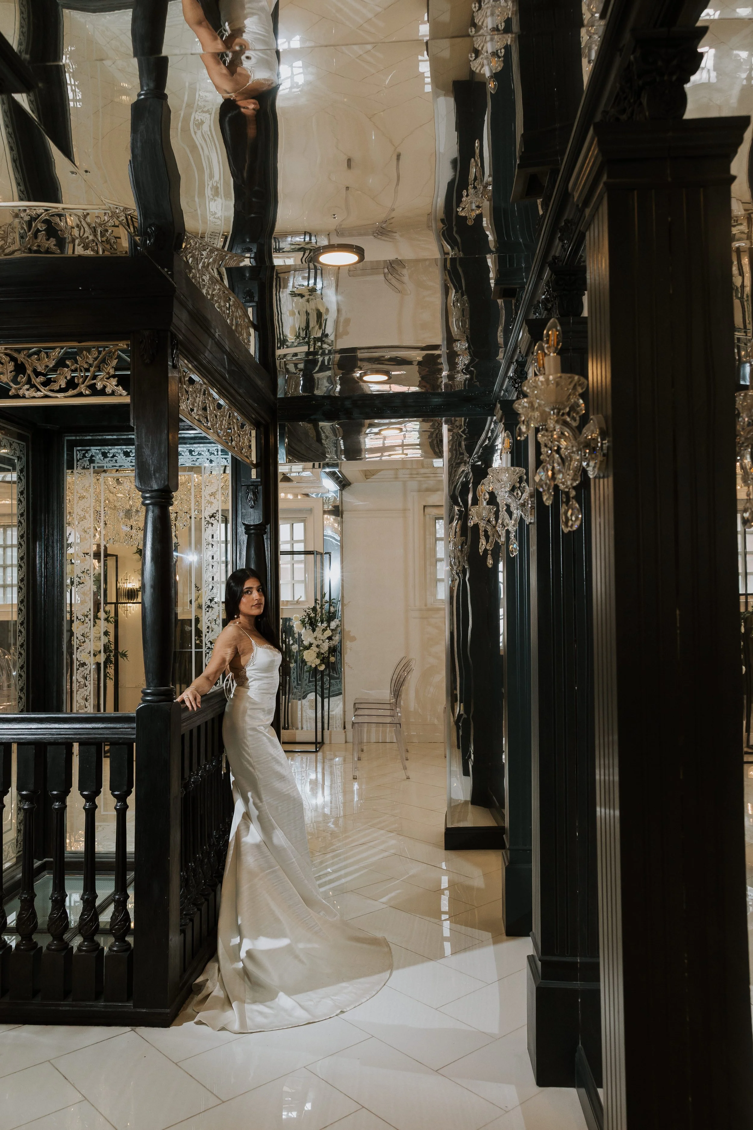 A bride in a white wedding dress standing in an elegant, luxurious interior with black and gold accents, chandeliers, and high ceilings.
