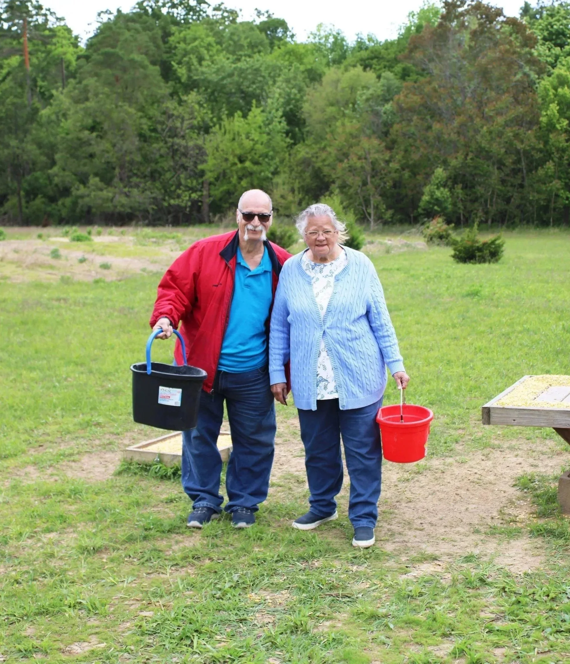 Riverwood tenants standing outdoors on grass, smiling and holding buckets at a deer feeder area.