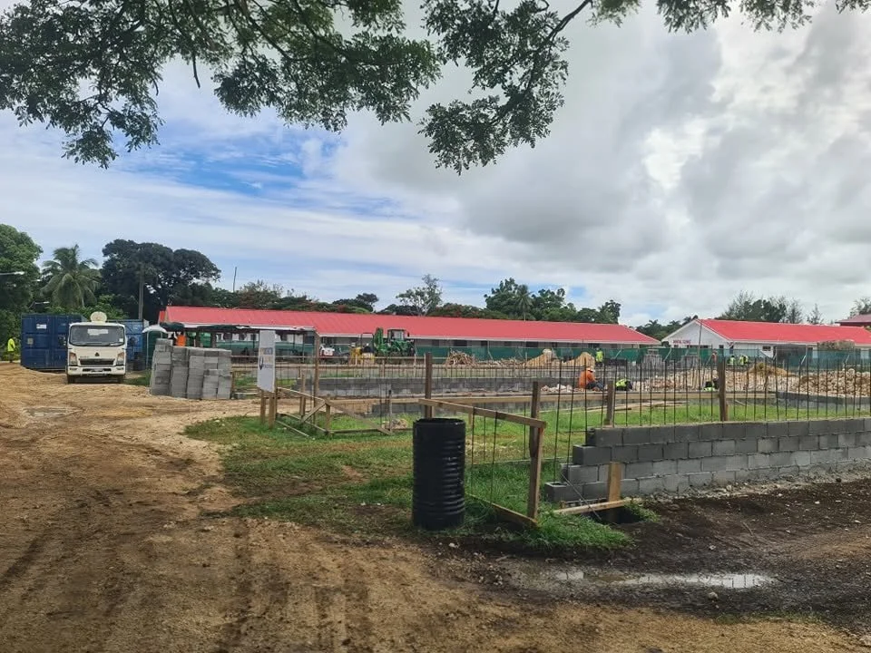 Construction site with building foundations, workers, construction materials, and equipment under a partly cloudy sky.