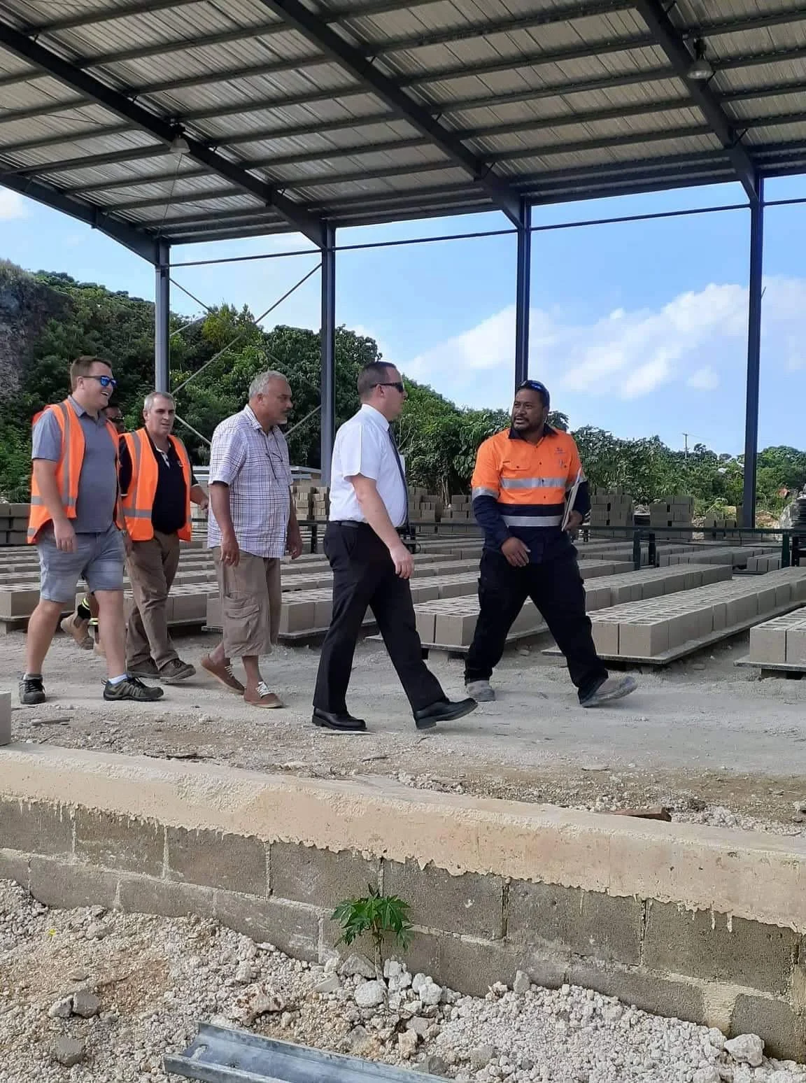 Group of men touring a construction site with concrete blocks and a partially completed structure.